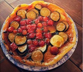 Una tarta salada de verduras con tomates cherry asados ​​y calabacín en rodajas sobre una base dorada, servida en un plato estampado.