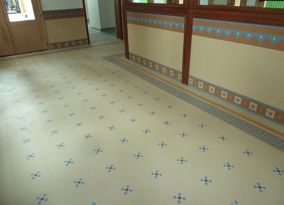 Sol carrelé à motifs de croix bleues, murs beiges à bordures décoratives et cloisons en bois.