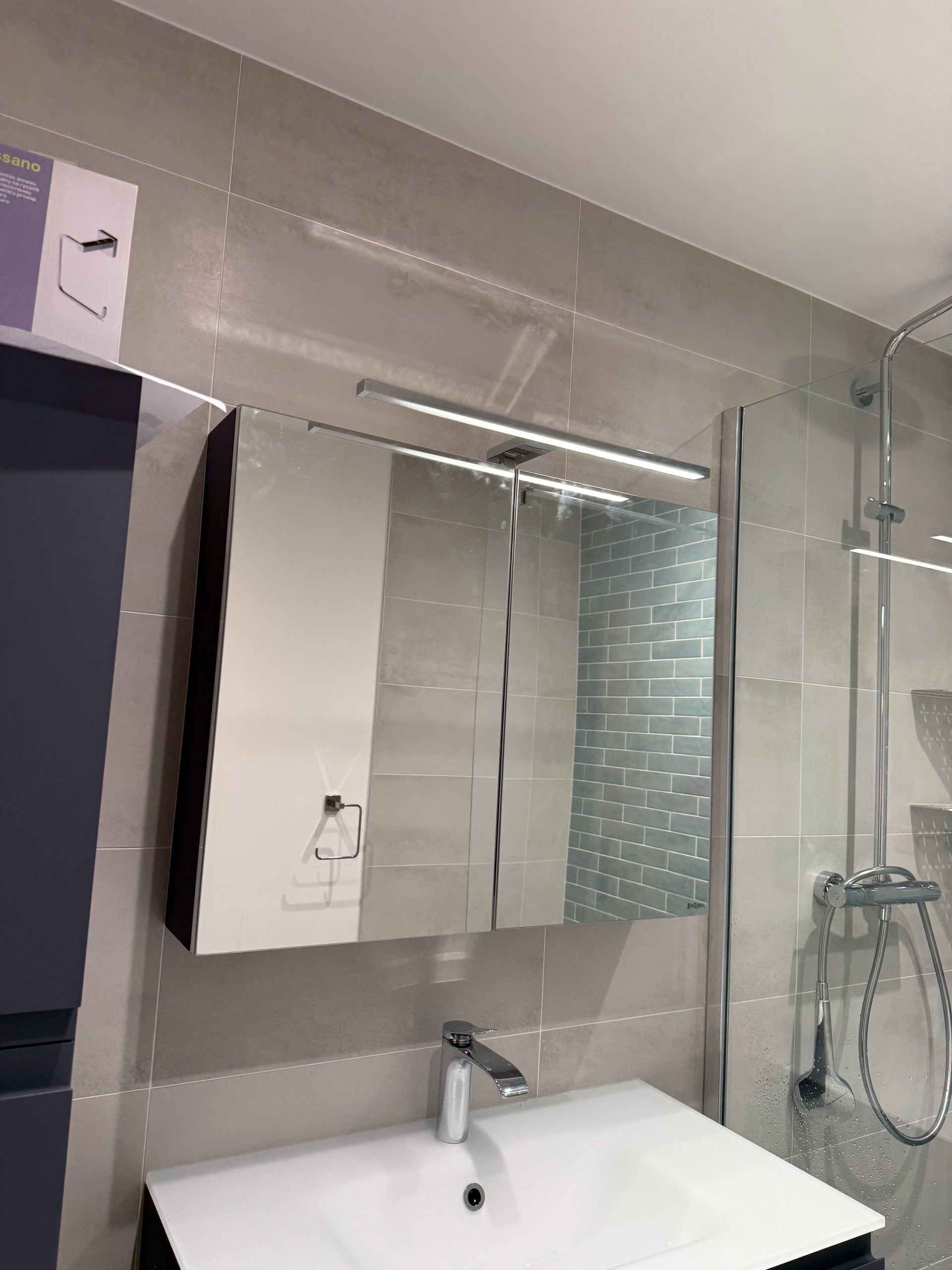 Salle de bain avec armoire à glace, lavabo, douche et murs carrelés gris.