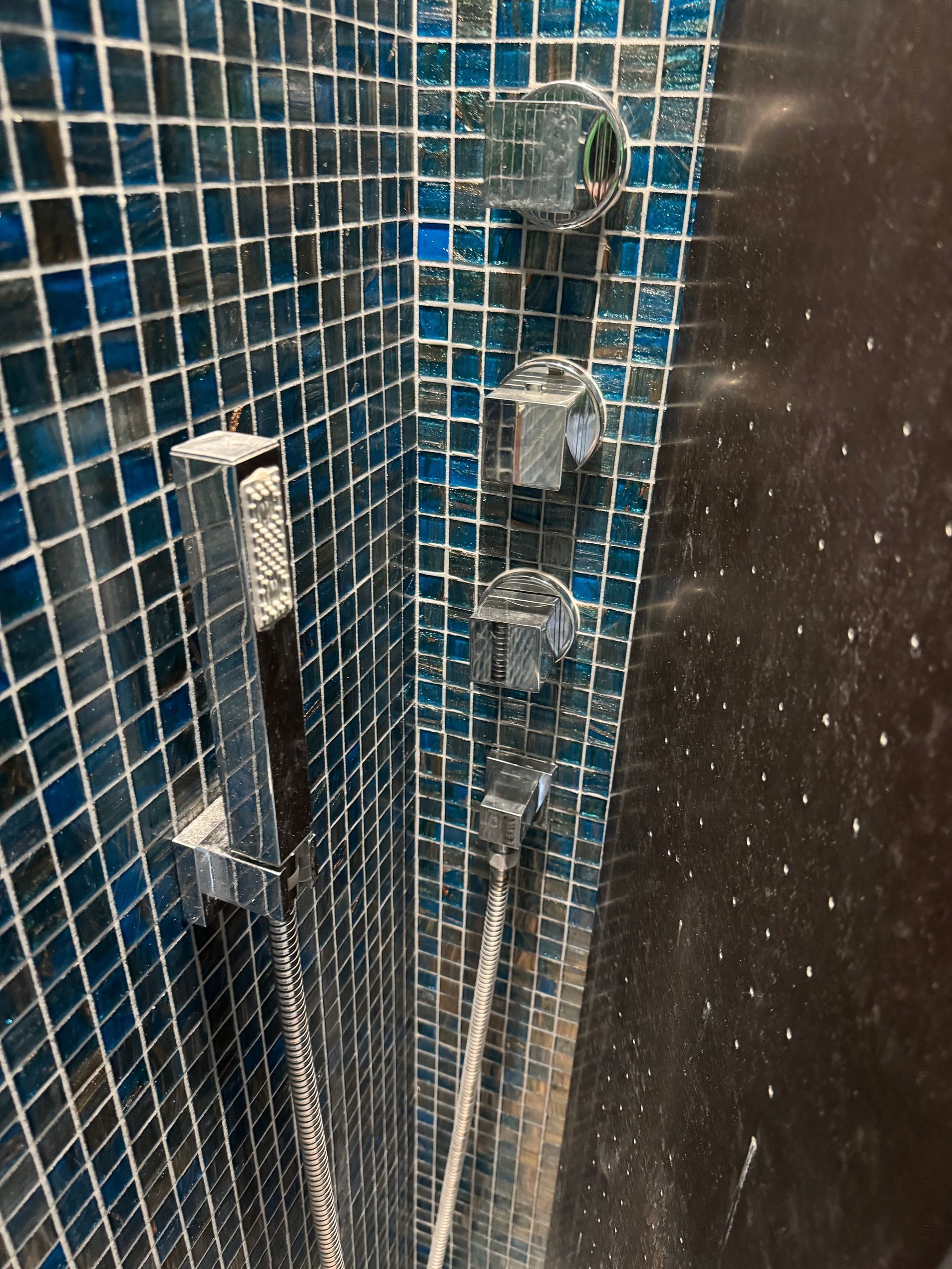 Douche carrelée bleue avec accessoires chromés; douche à main et trois commandes.