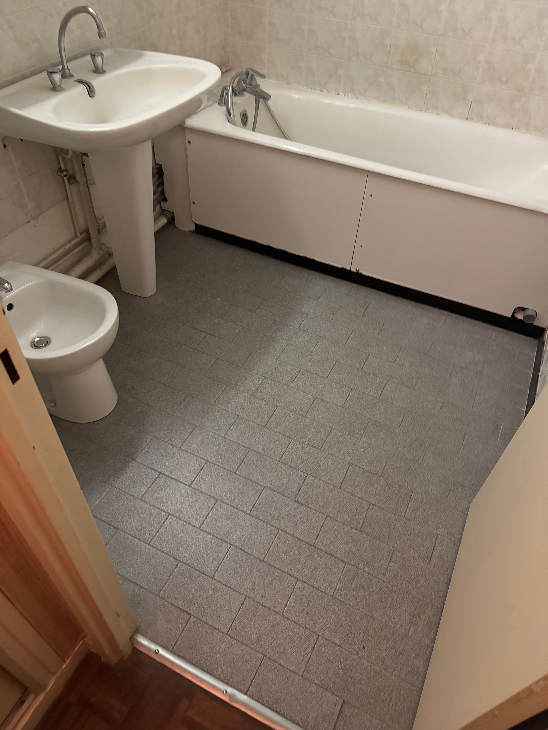 Salle de bain avec lavabo, baignoire et bidet. Sol carrelé gris.