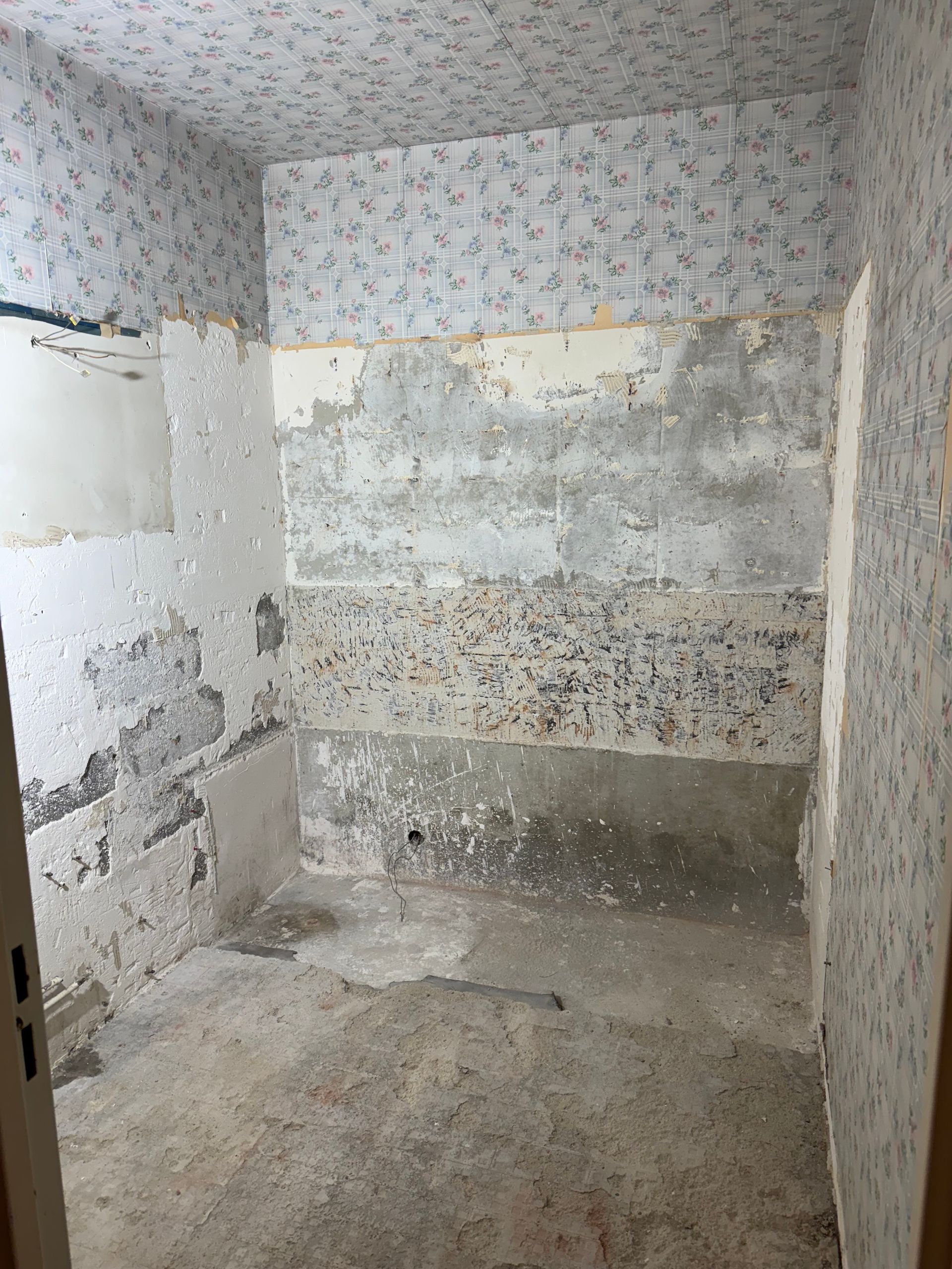 Une petite salle de bains avec du papier peint qui se décolle, montrant des dégâts des eaux et des travaux de construction.