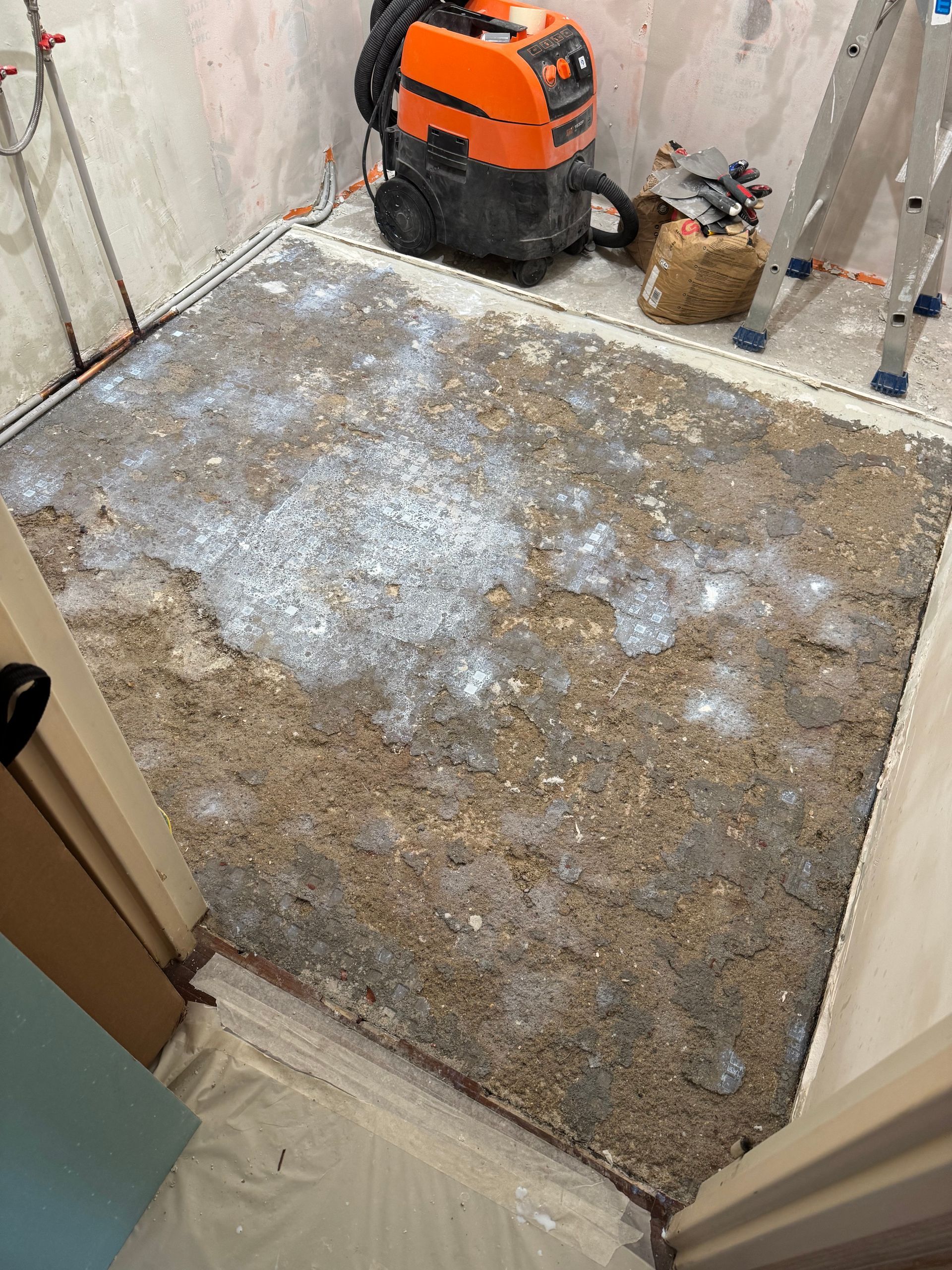 Une pièce avec un sol brut et non fini, des outils de construction et un aspirateur.