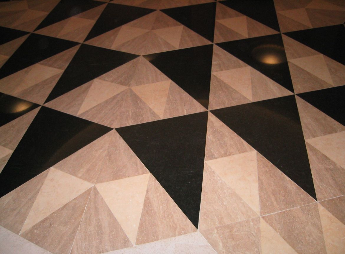 Carreaux de sol à motifs géométriques en noir et beige, créant un design triangulaire.