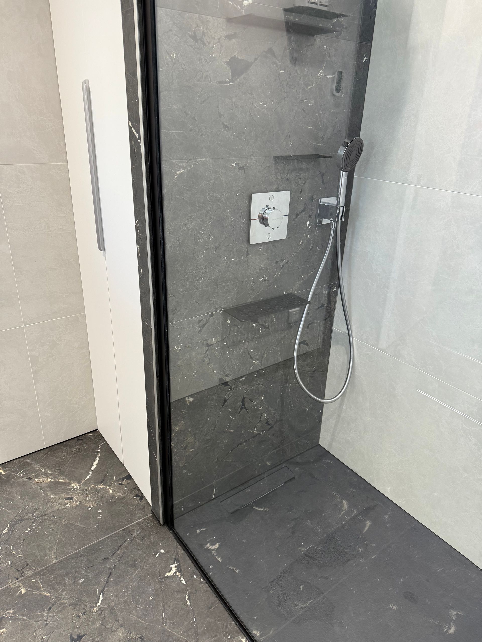 Douche avec carrelage foncé et paroi vitrée