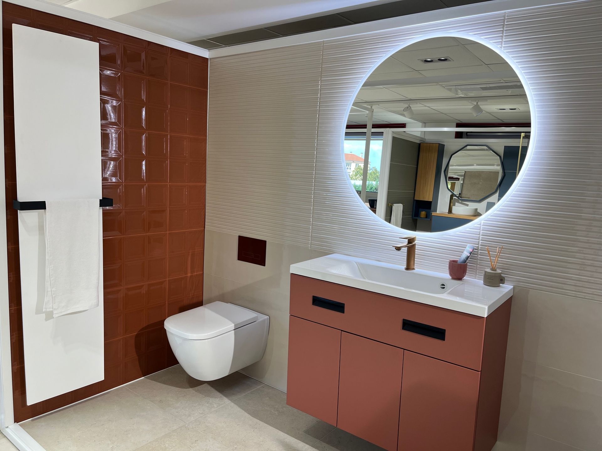 Salle de bain avec murs en terre cuite, luminaires blancs et miroir rond éclairé.