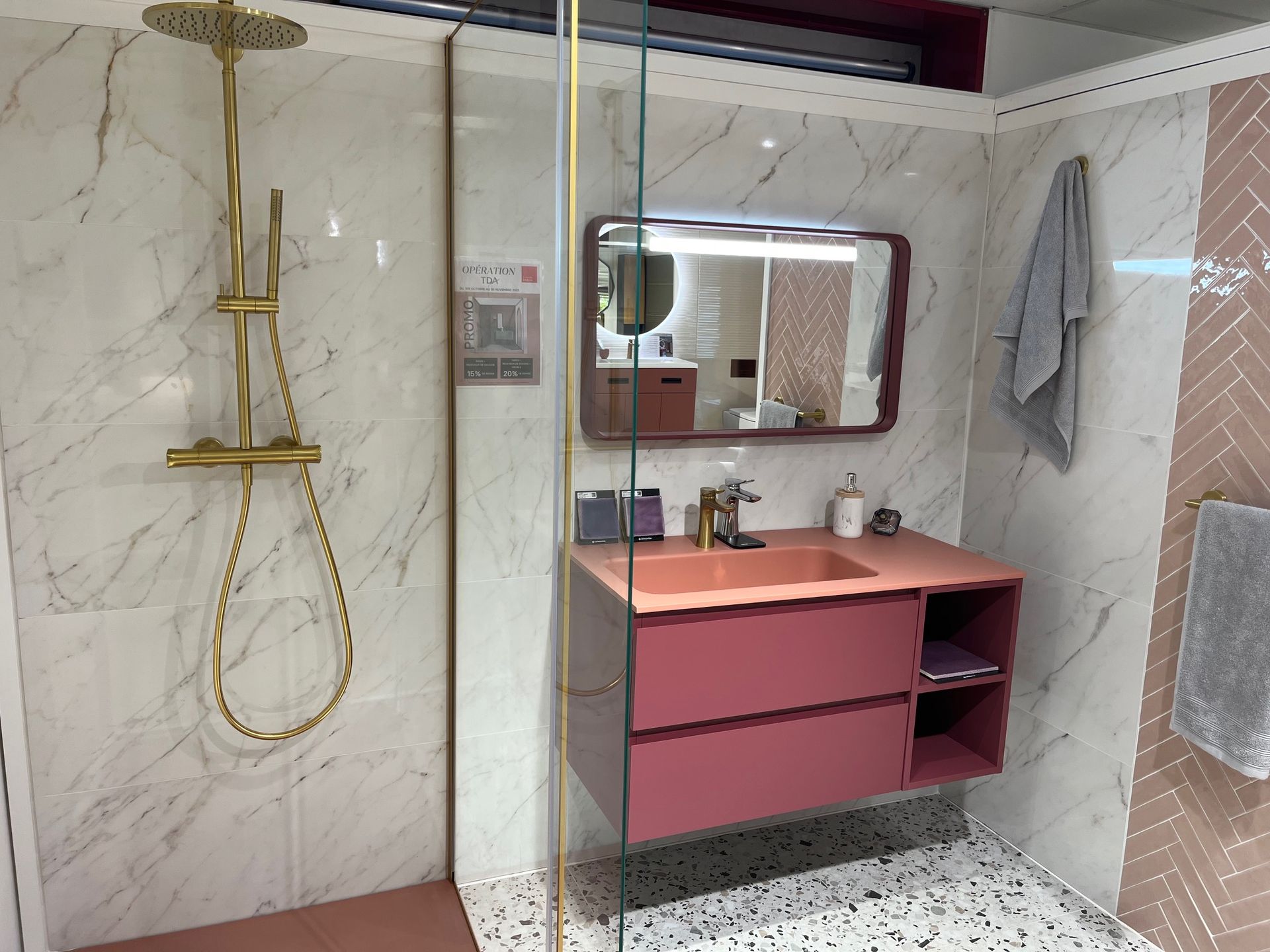 Salle de bain avec vanité rose, accessoires de douche dorés et carrelage en marbre et à chevrons.