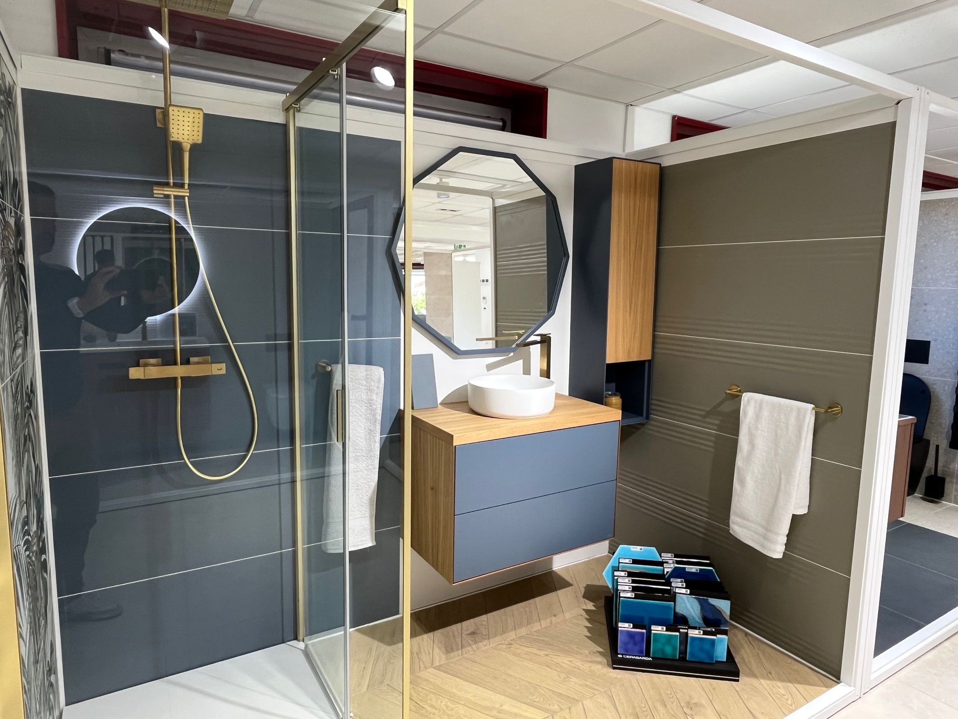 Salle de bain moderne aux tons gris, bleu et bois. Douche, meuble-lavabo avec miroir octogonal et étagères.