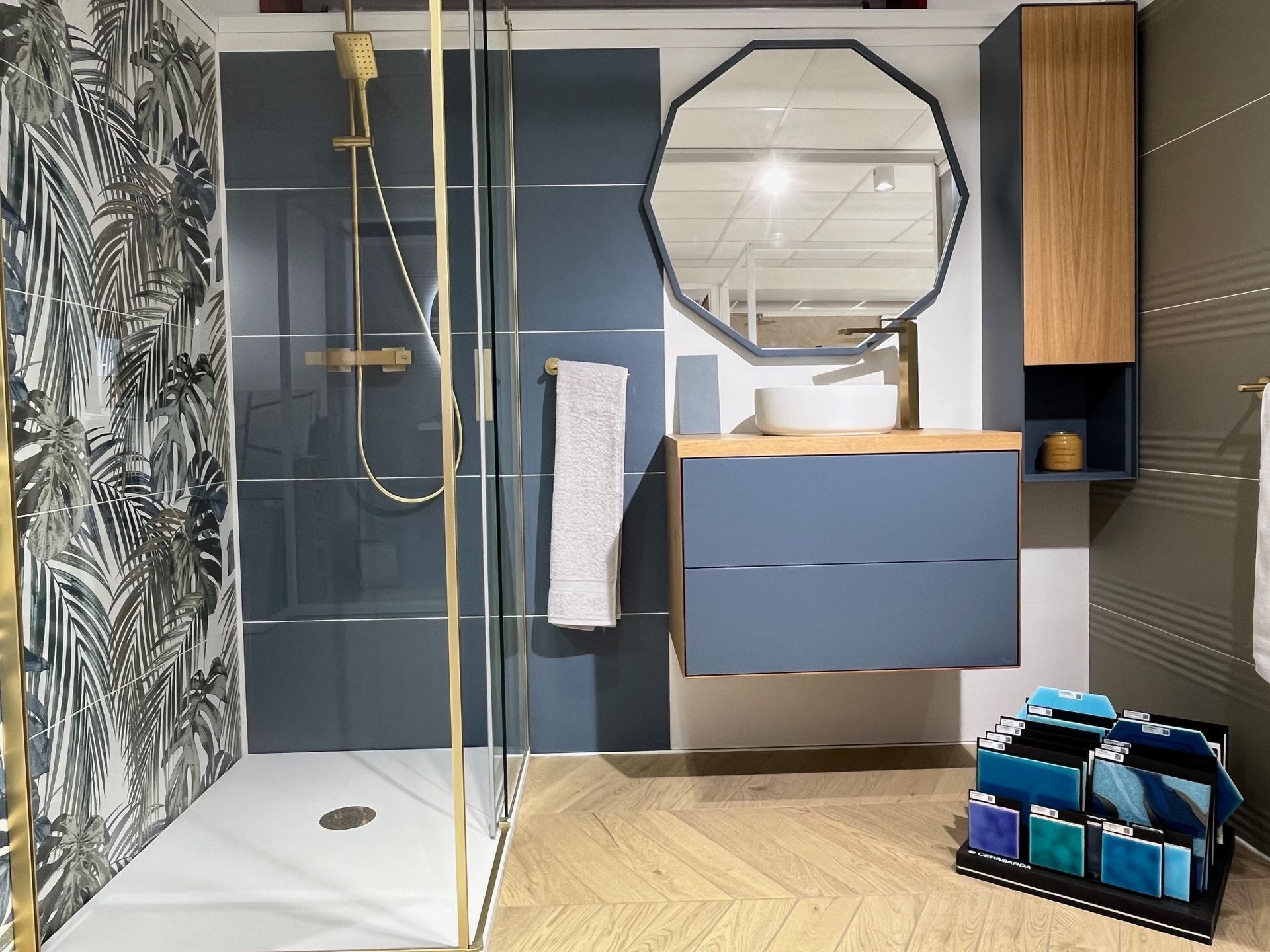Salle de bain moderne avec douche, vanité bleue, papier peint à motifs, plancher en bois.