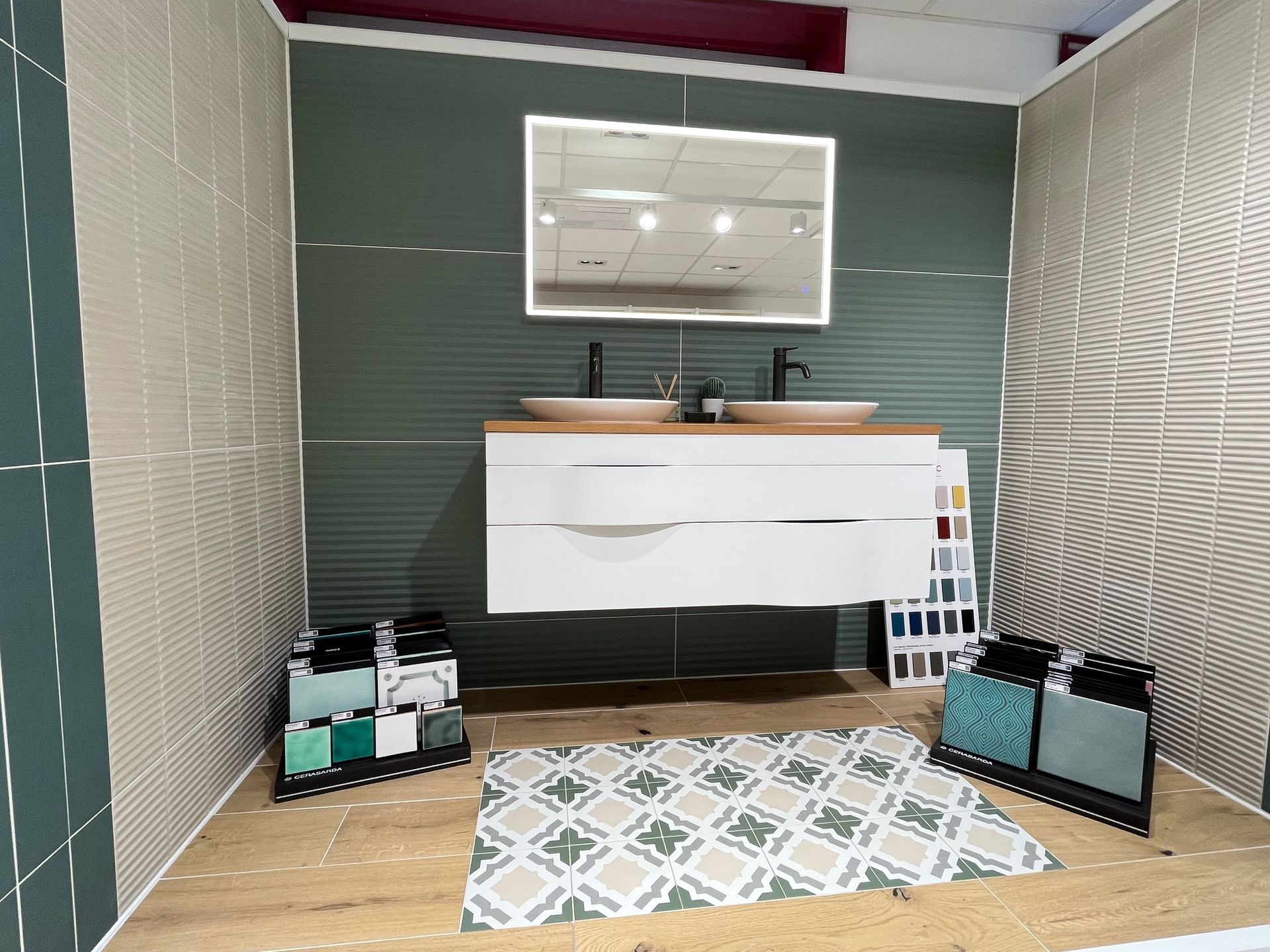 Présentoir de salle de bain avec vanité blanche, mur vert, miroir éclairé et tapis à motifs.