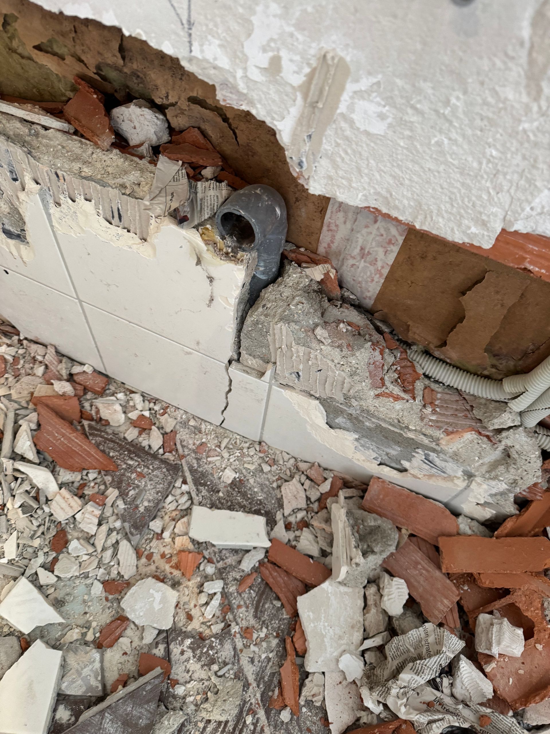Tuyaux et gravats au sol après démolition d’un mur