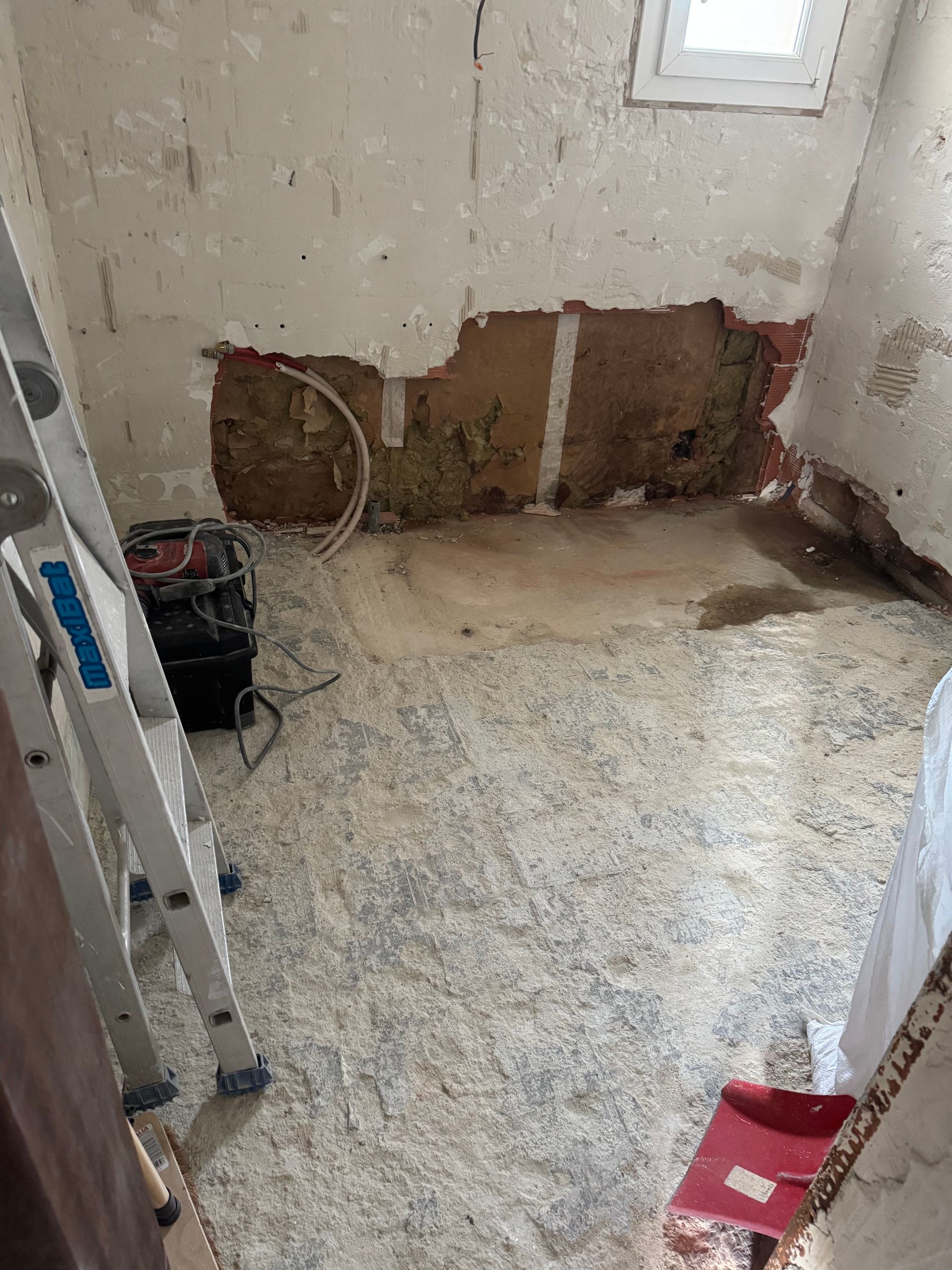 Mur dégagé avec anciennes canalisations visibles et sol brut