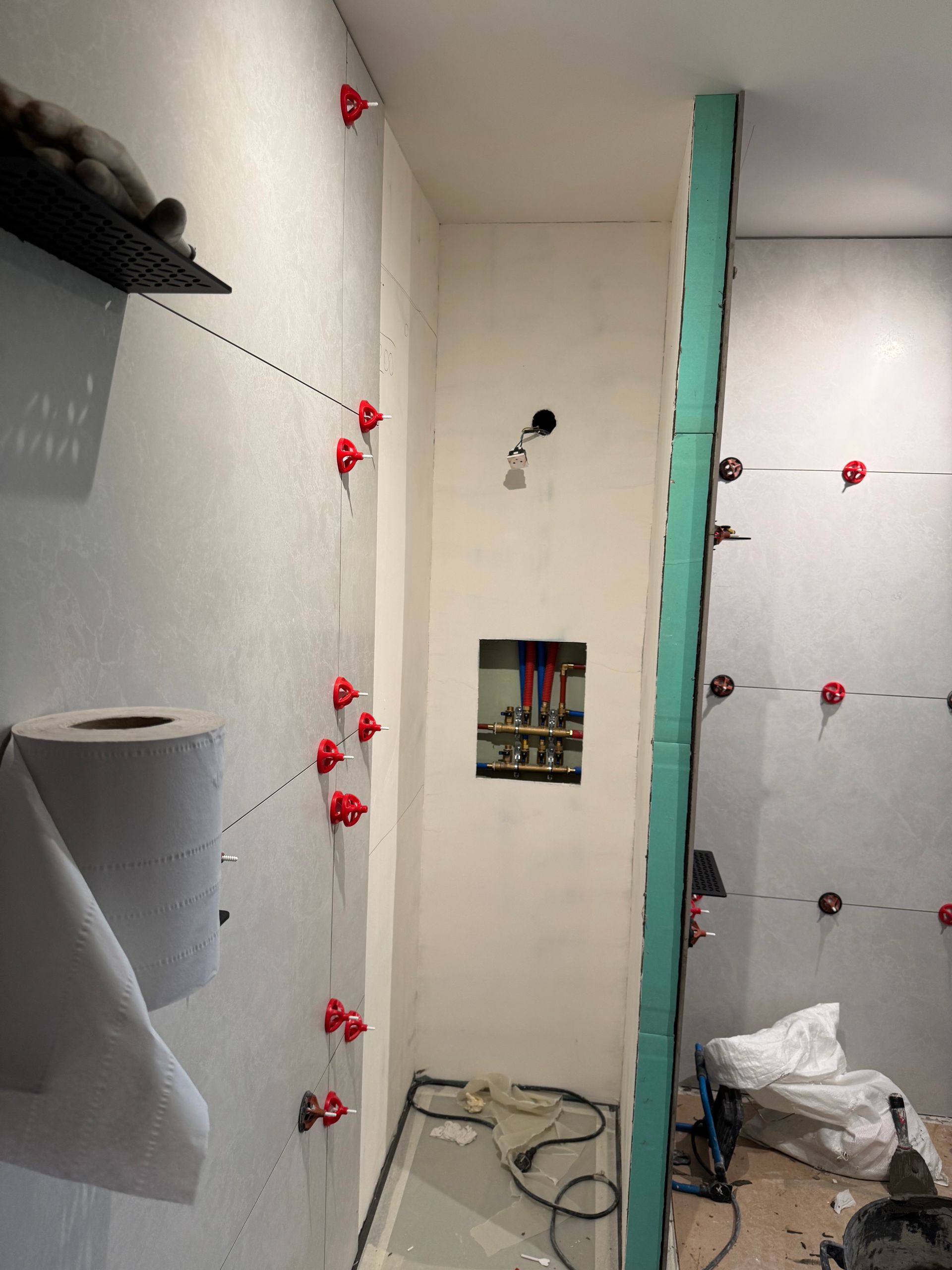 Salle de bains en construction ; carrelage partiellement posé, attaches de nivellement rouges visibles.