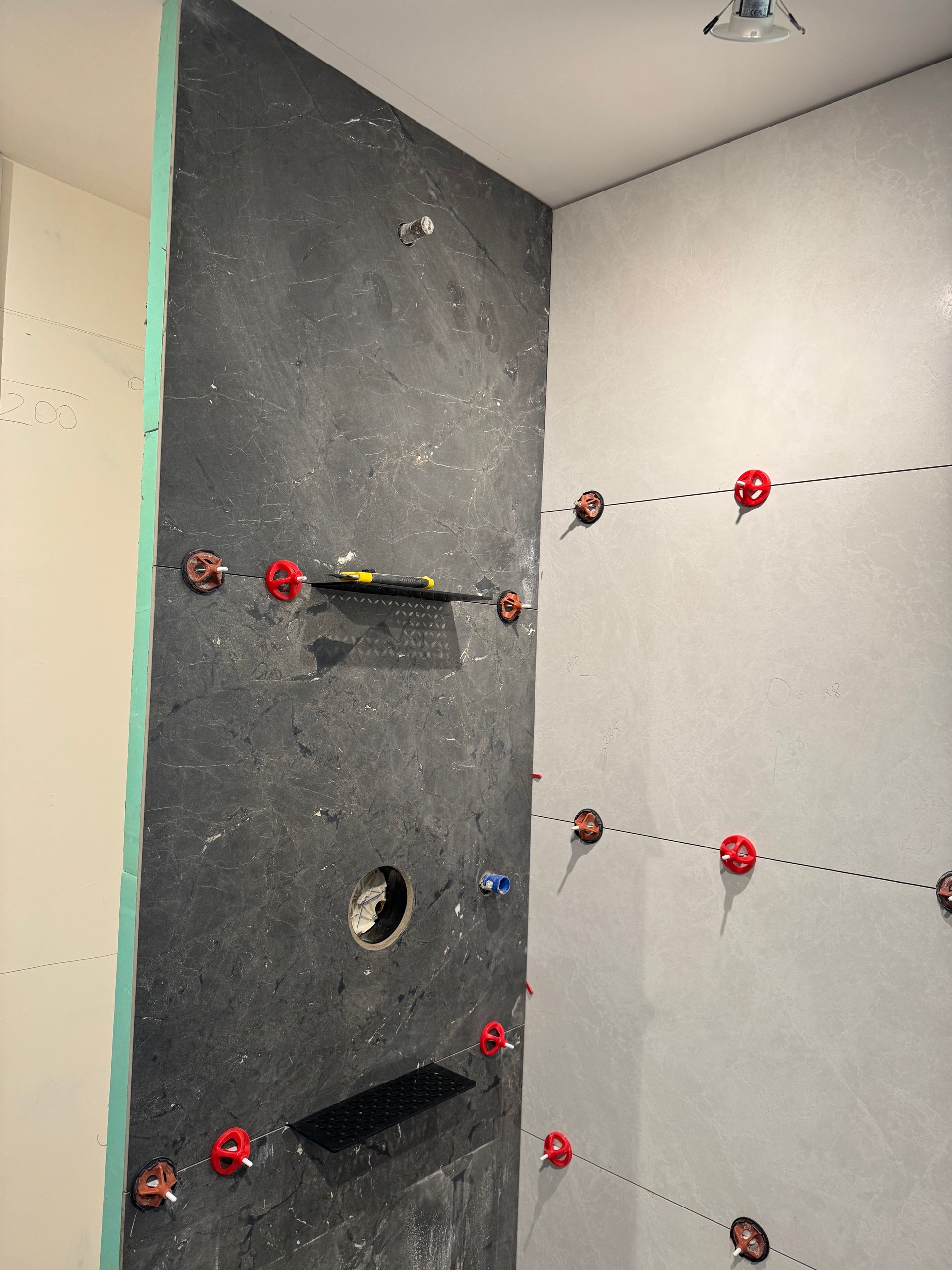 Cabine de douche en construction, carrelage foncé, clips de nivellement, accessoires de douche.