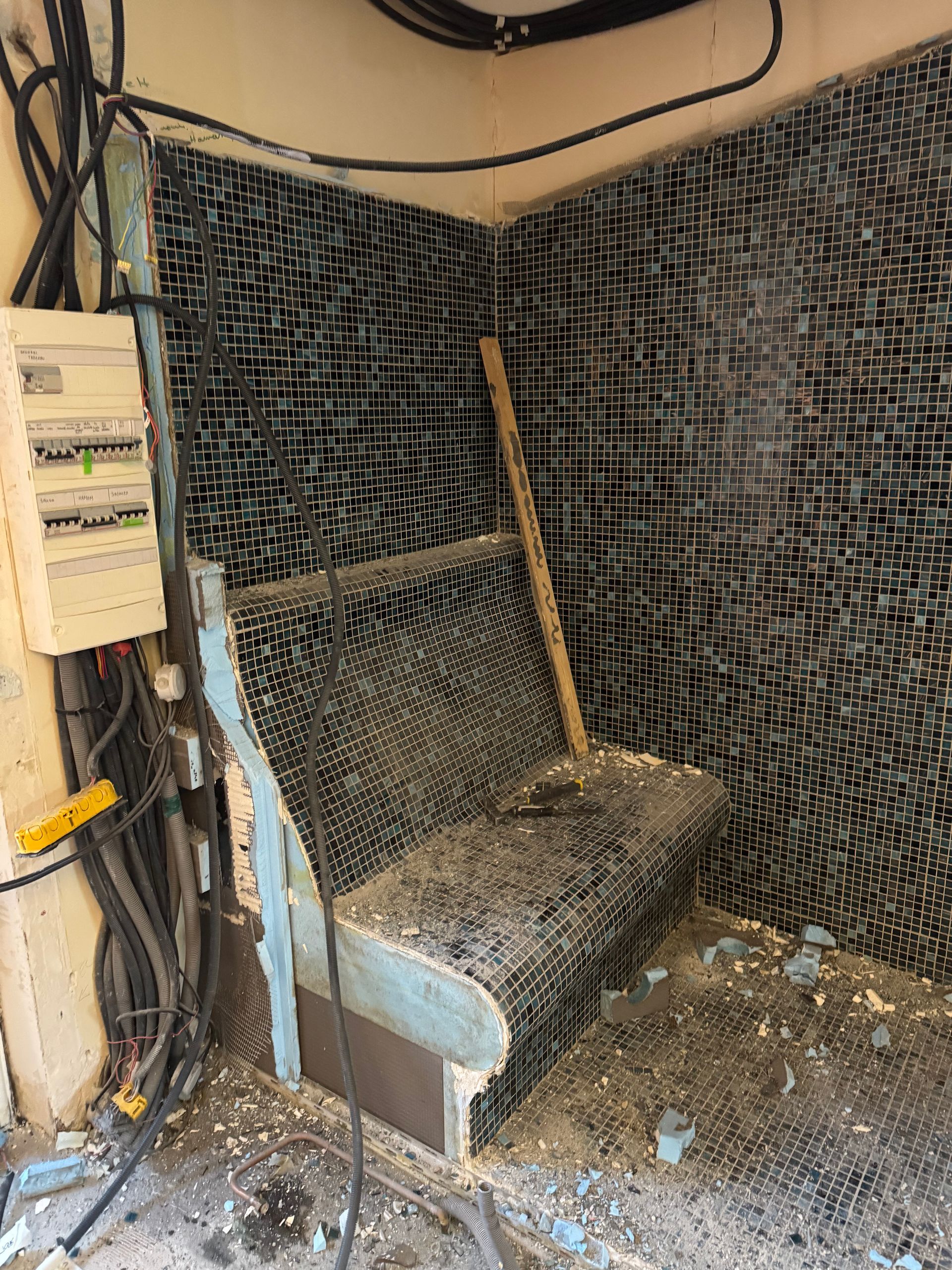 Un banc d'angle endommagé en treillis noir. Panneau électrique et fils à proximité.