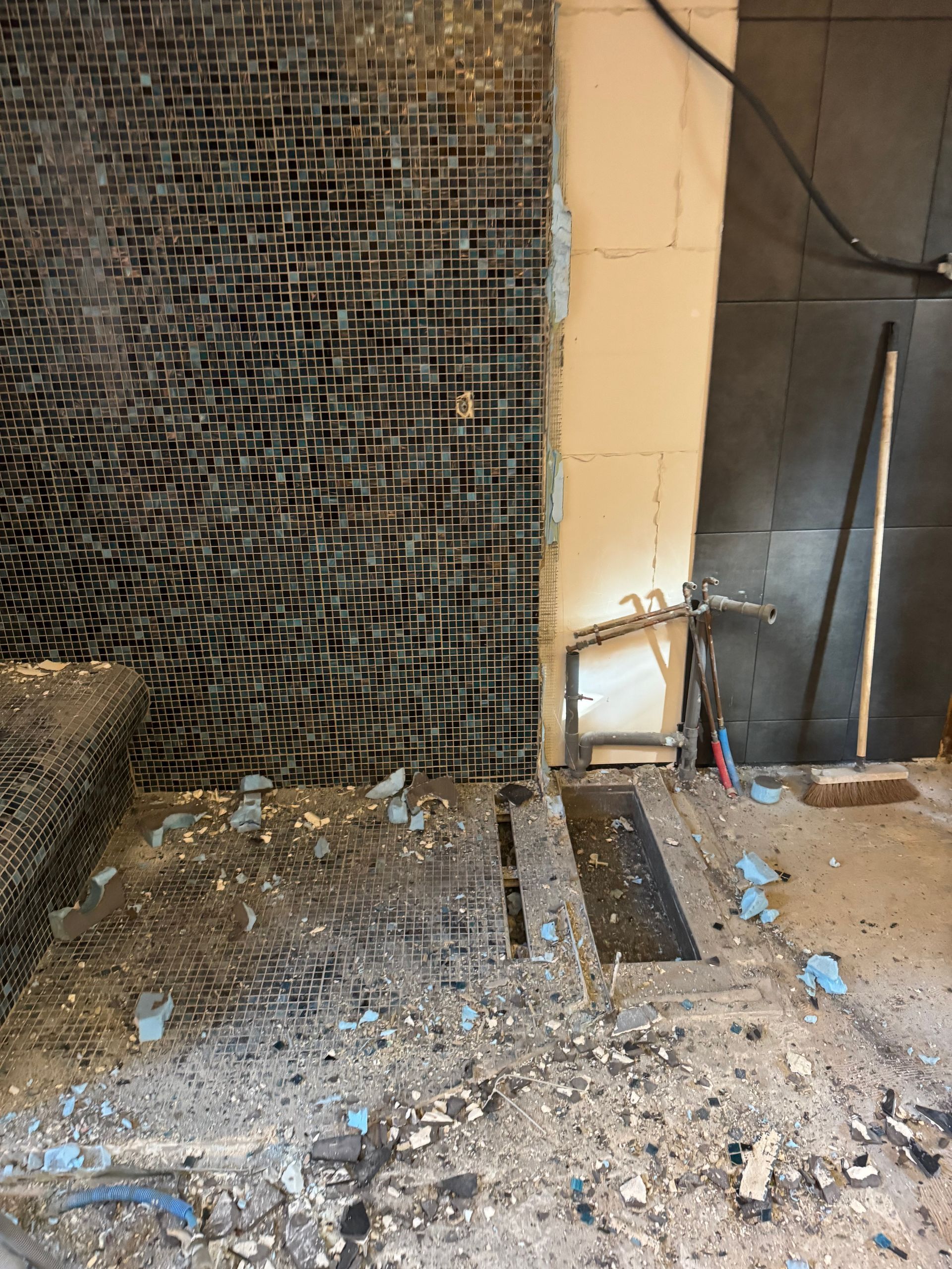 Chantier de construction. Grillage métallique sur les murs et le sol, débris, tuyaux apparents, drain de douche.