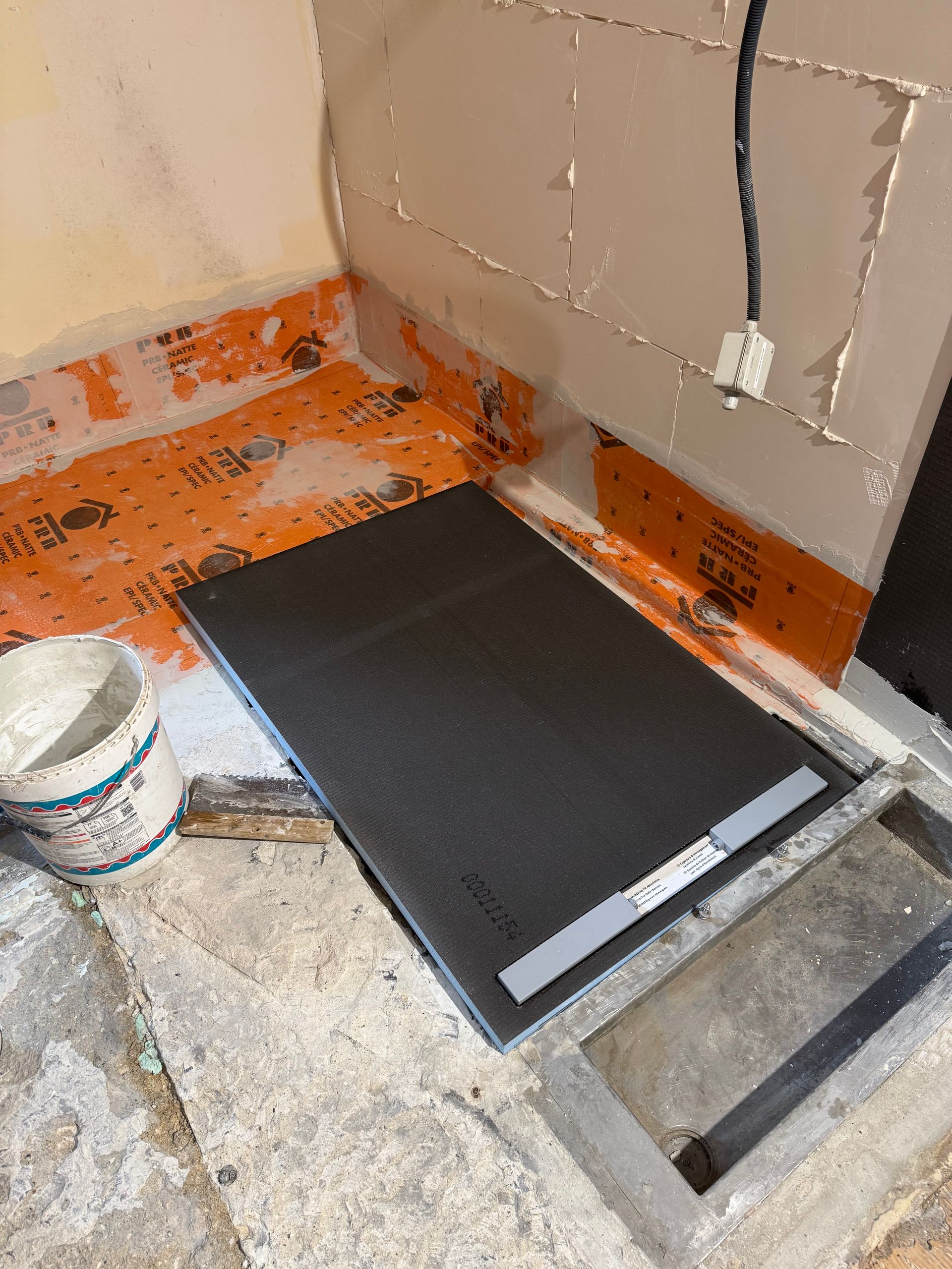 Construction du plancher de douche : base en mousse noire installée, ruban d'étanchéité orange sur les murs et le sol.