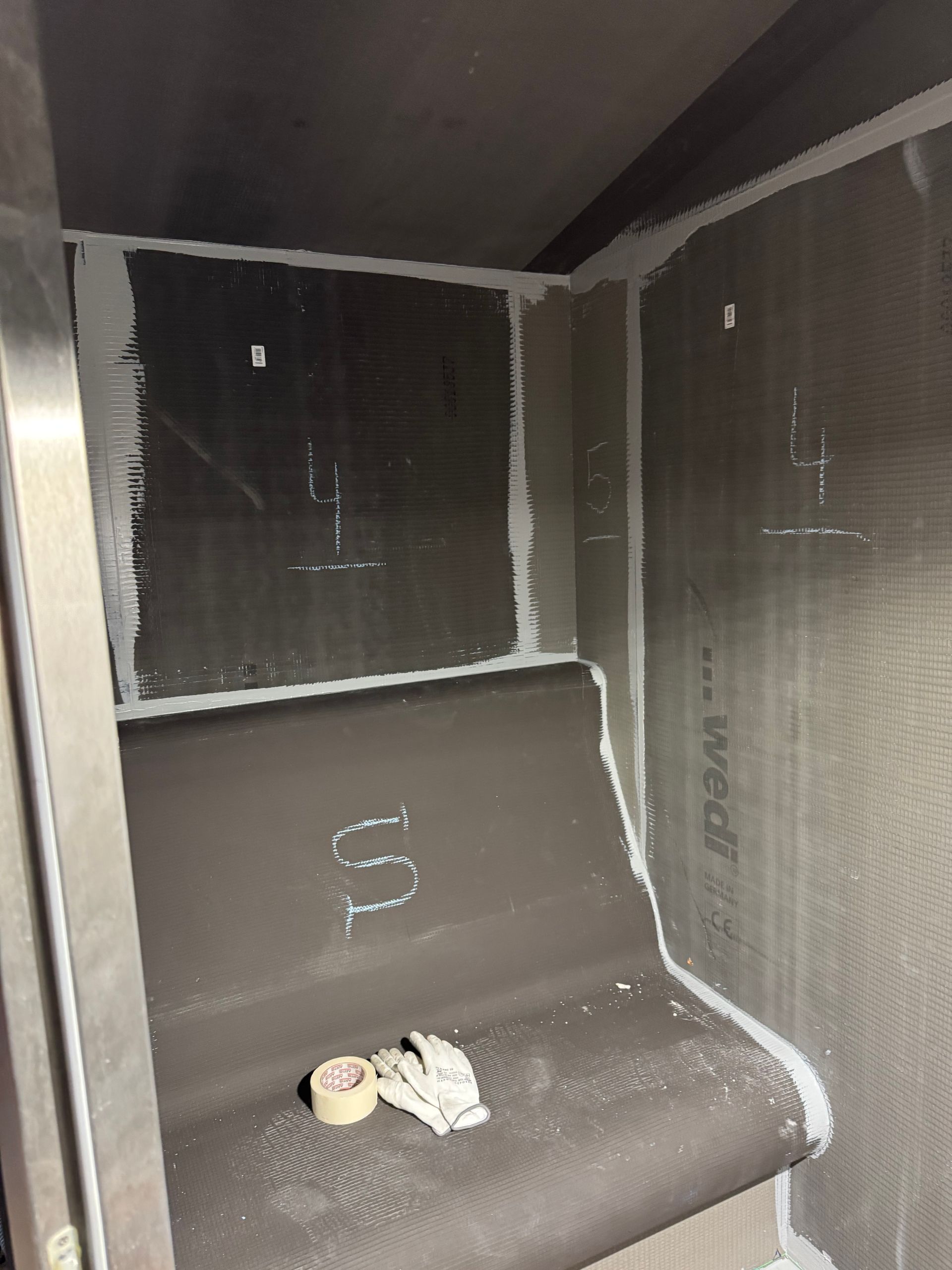 Une douche partiellement construite avec des panneaux imperméables gris et un mastic blanc.