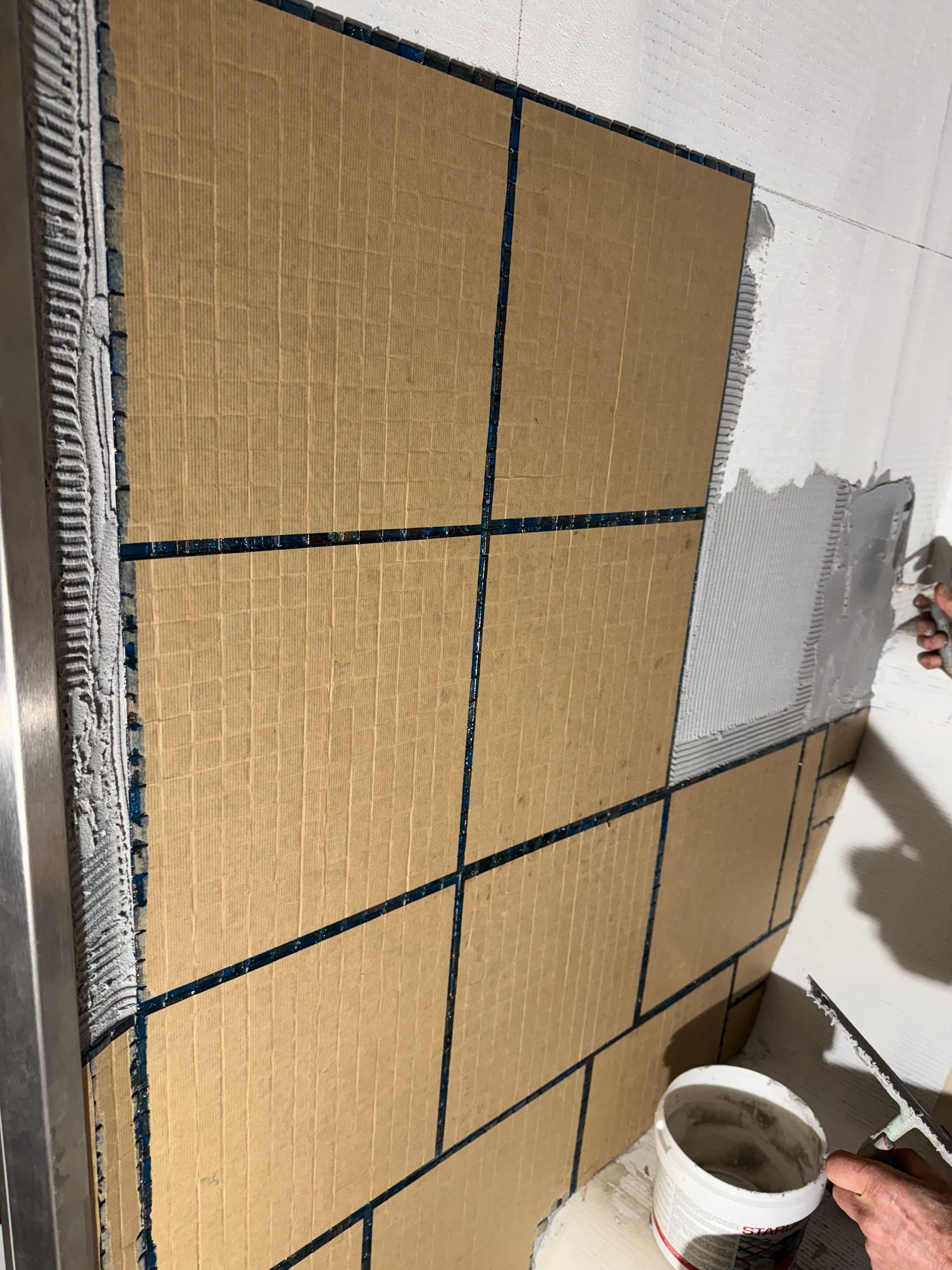 Pose de grands carreaux marron avec coulis foncé sur un mur blanc.