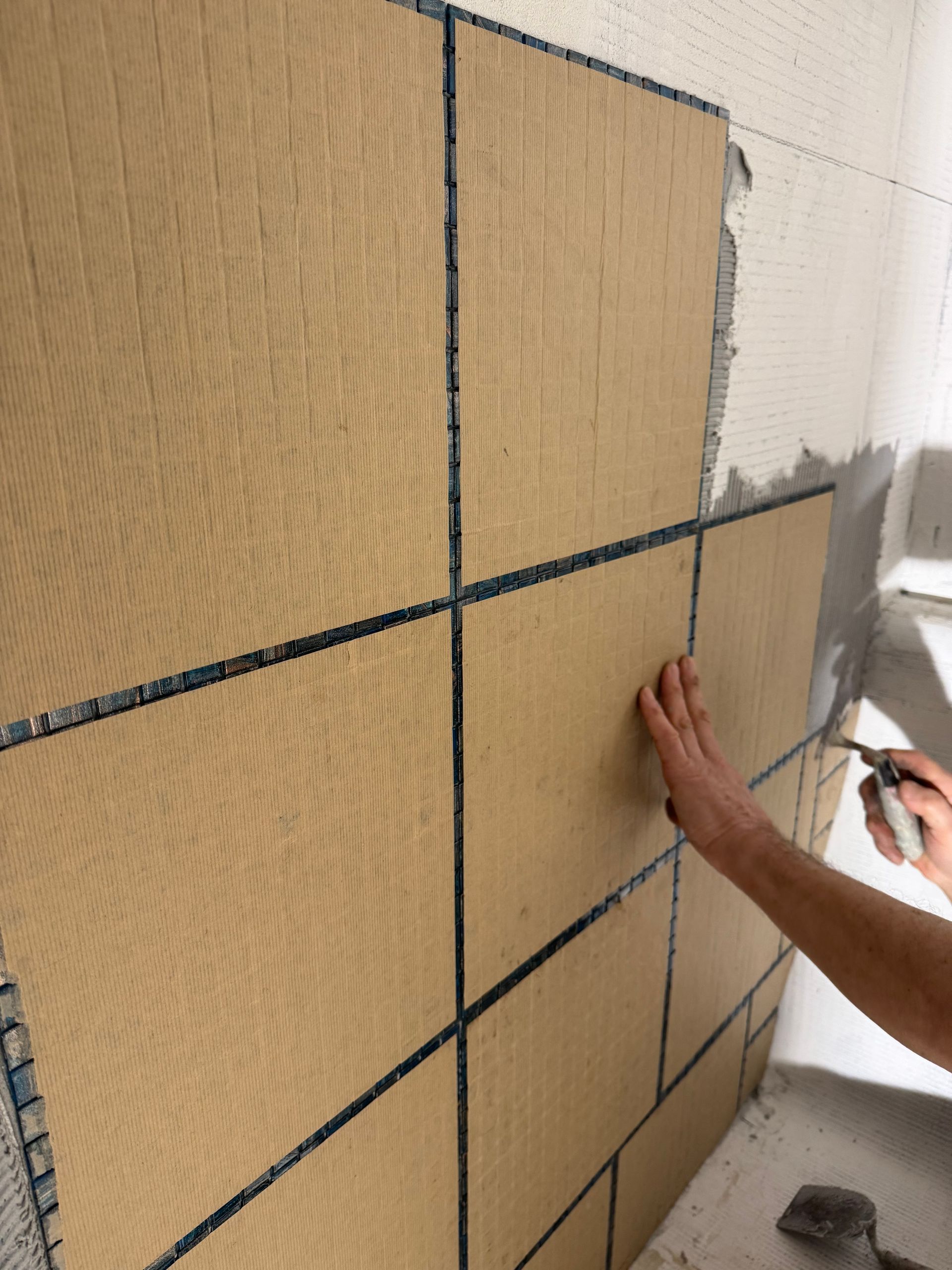 Personne carrelant un mur avec de grands carreaux carrés beiges, appliquant du coulis.