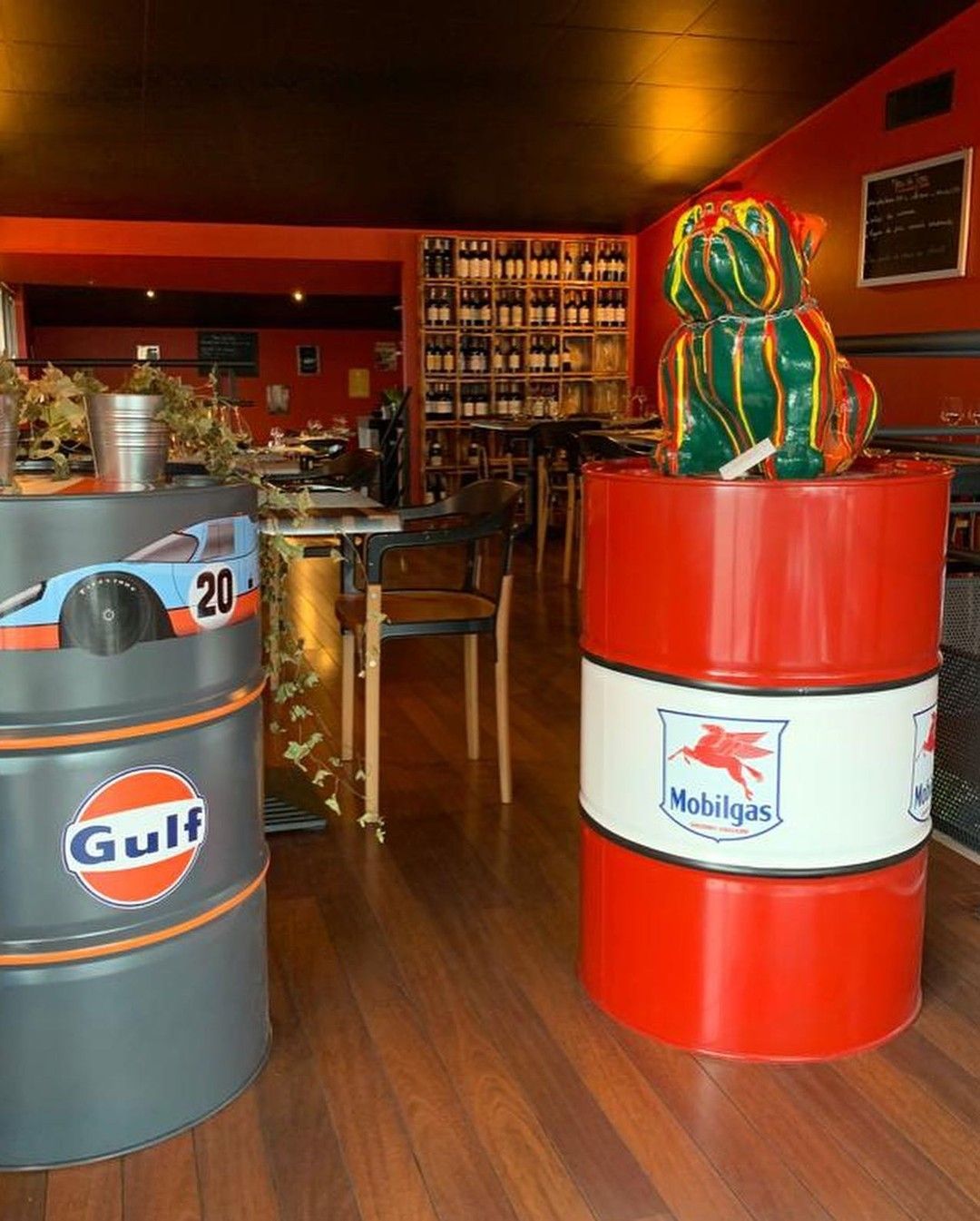 Intérieur du restaurant avec décor de bidons d'huile, une statue de bouledogue colorée et des bouteilles sur des étagères.
