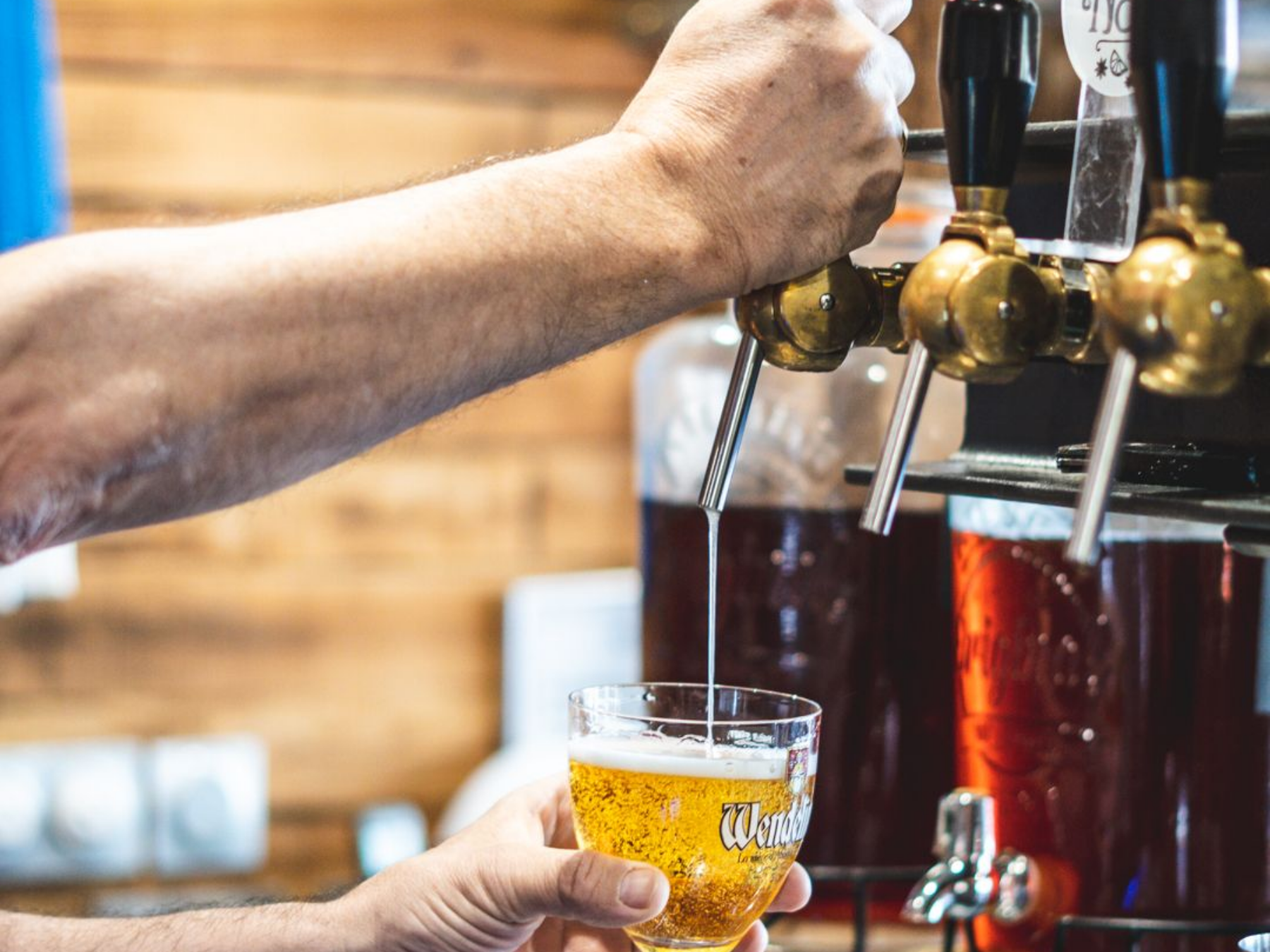 Personne versant une bière pression dans un verre, ambiance bar.