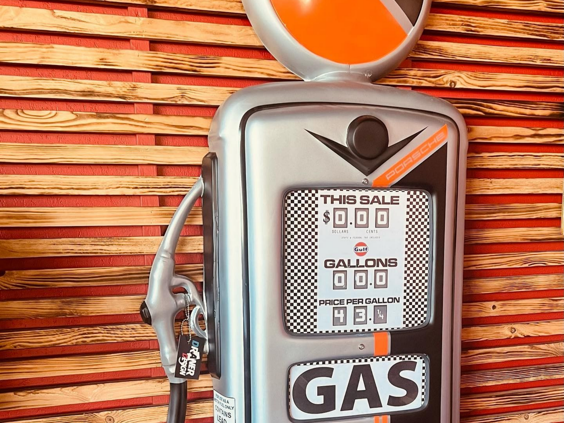 Décoration vintage de pompe à essence, argentée avec des touches orange, sur un mur lambrissé.