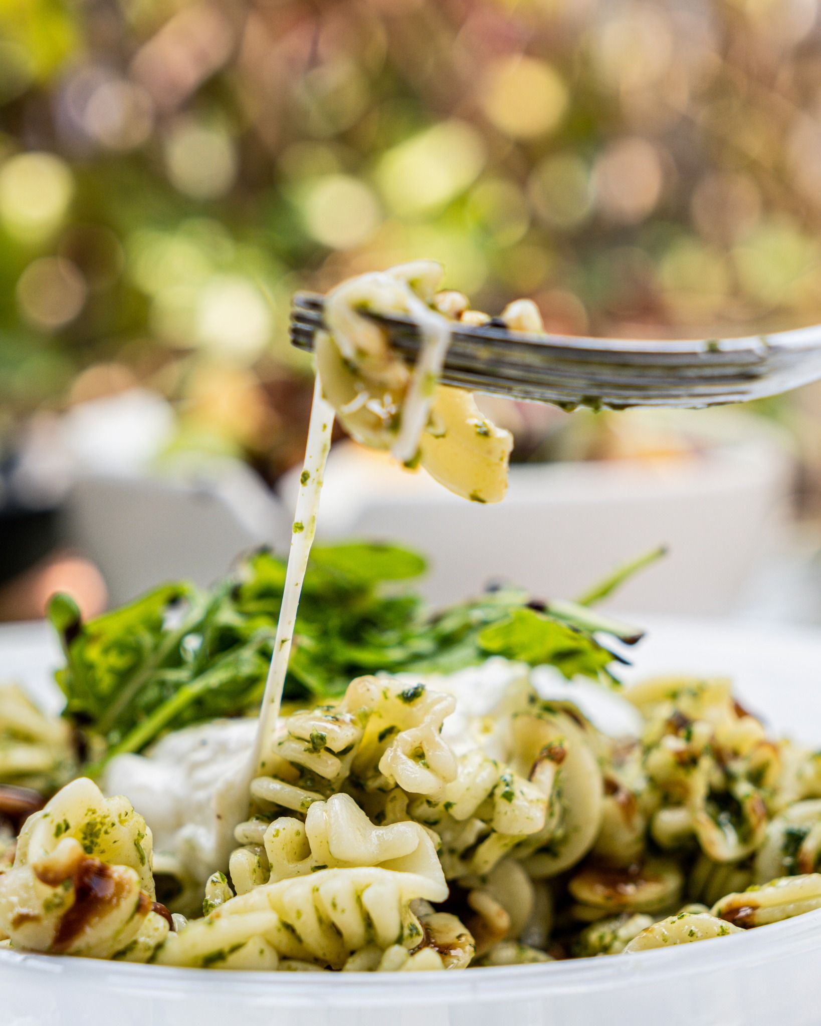 Plat de pâtes au pesto, aux légumes verts et au fromage, certaines pâtes étant soulevées à l'aide d'une fourchette.