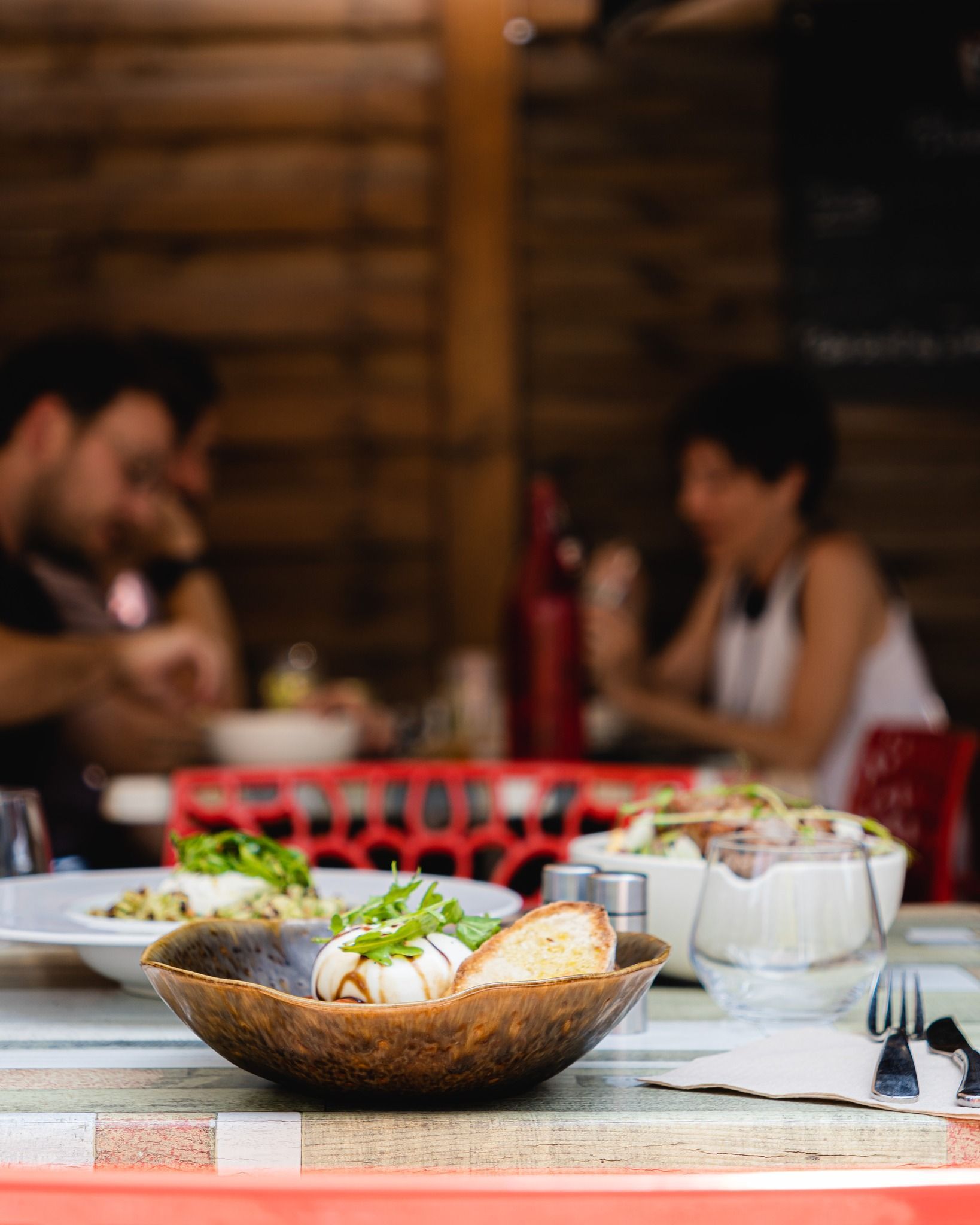 Table garnie ; un couple se devine en arrière-plan. Amuse-bouche servi dans un bol en bois.