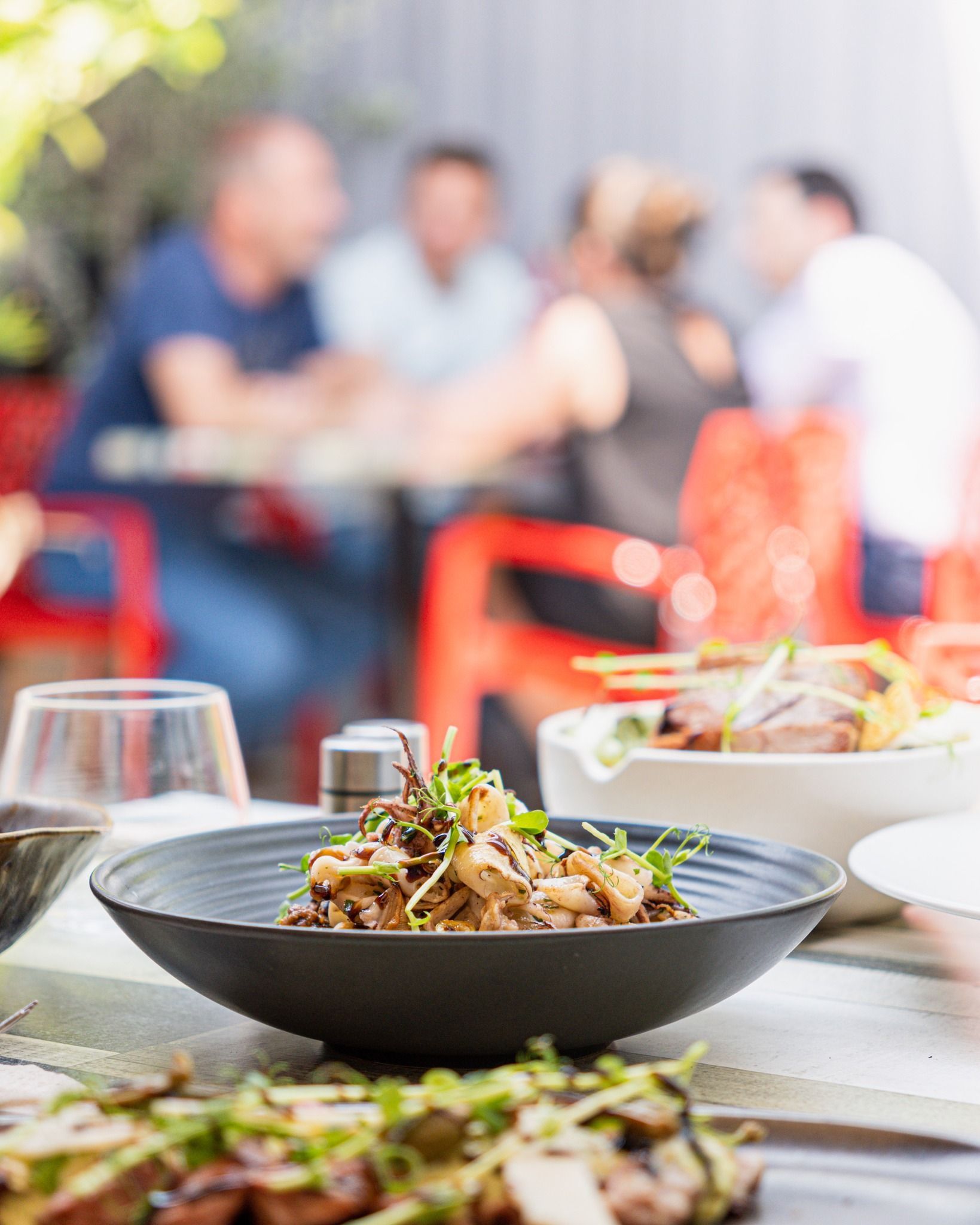 Un bol de nourriture noir sur une table avec des personnes floues assises dans un restaurant.