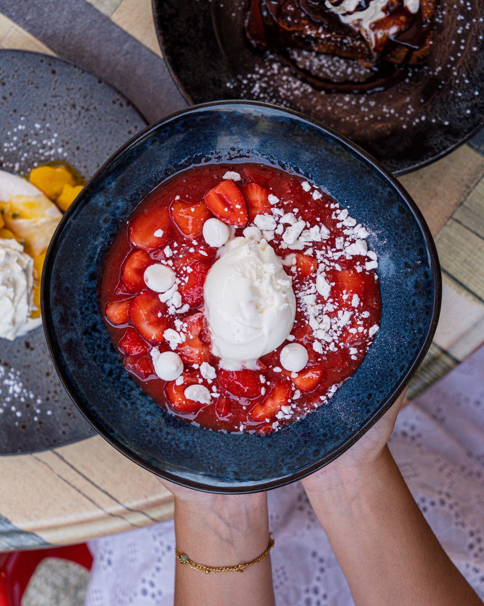 Un bol de fraises avec de la glace, posé au-dessus d'une table où se trouvent d'autres desserts.