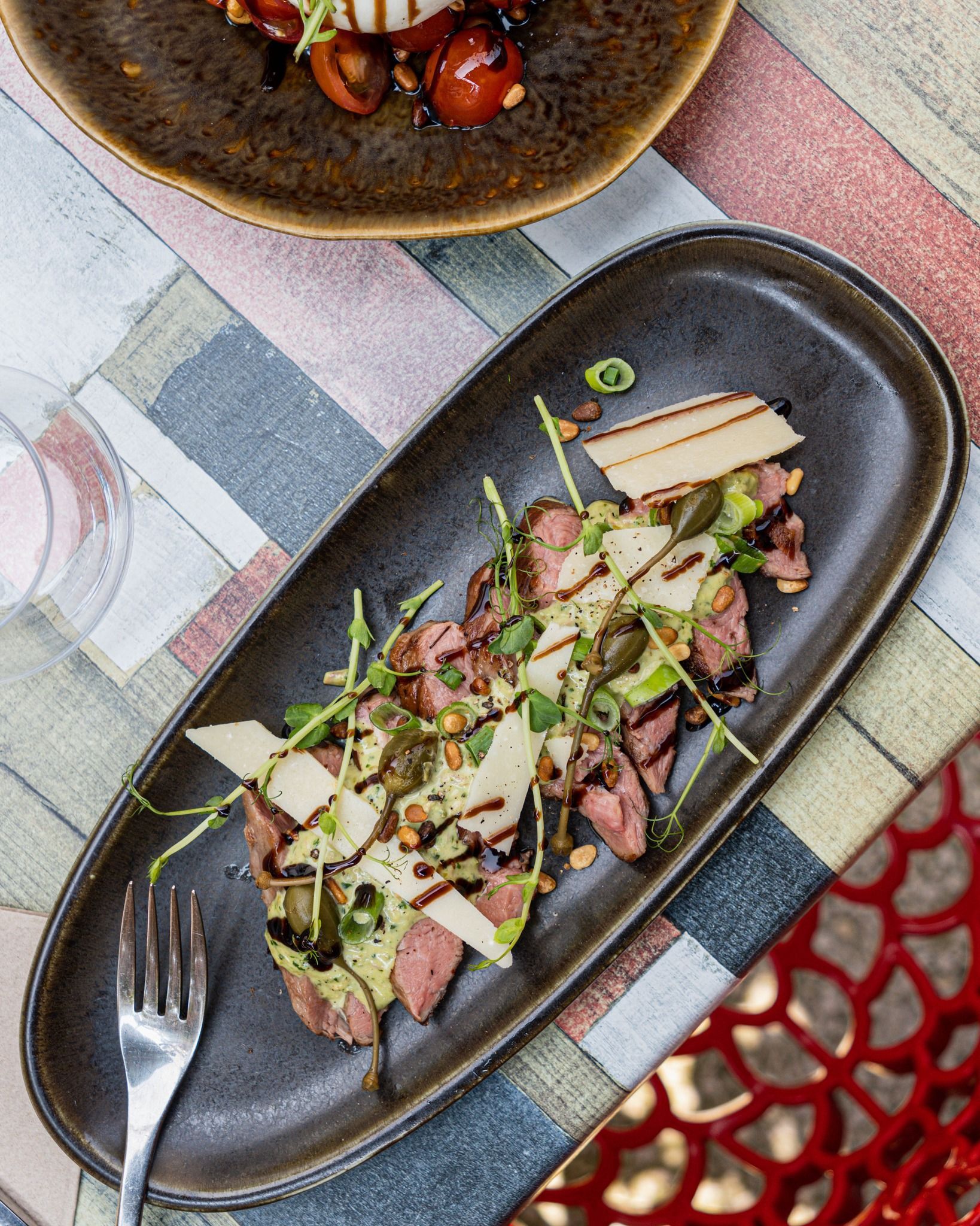 Salade de steak émincé avec fromage et sauce, servie dans une assiette oblongue foncée. Une fourchette est placée à gauche.