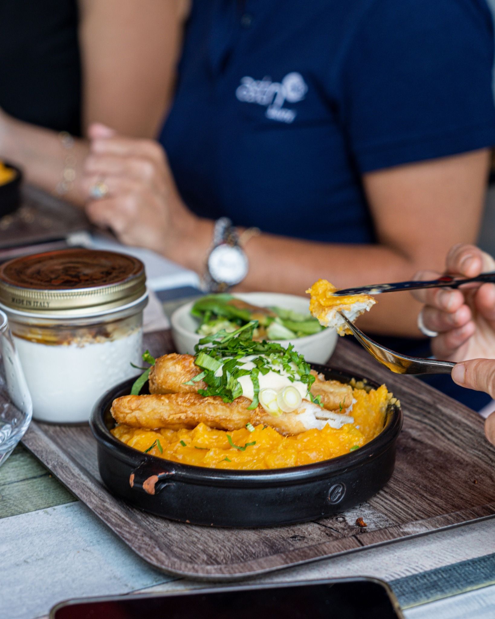 Une personne mangeant une assiette de purée de légumes avec des aliments frits, servie sur un plateau.
