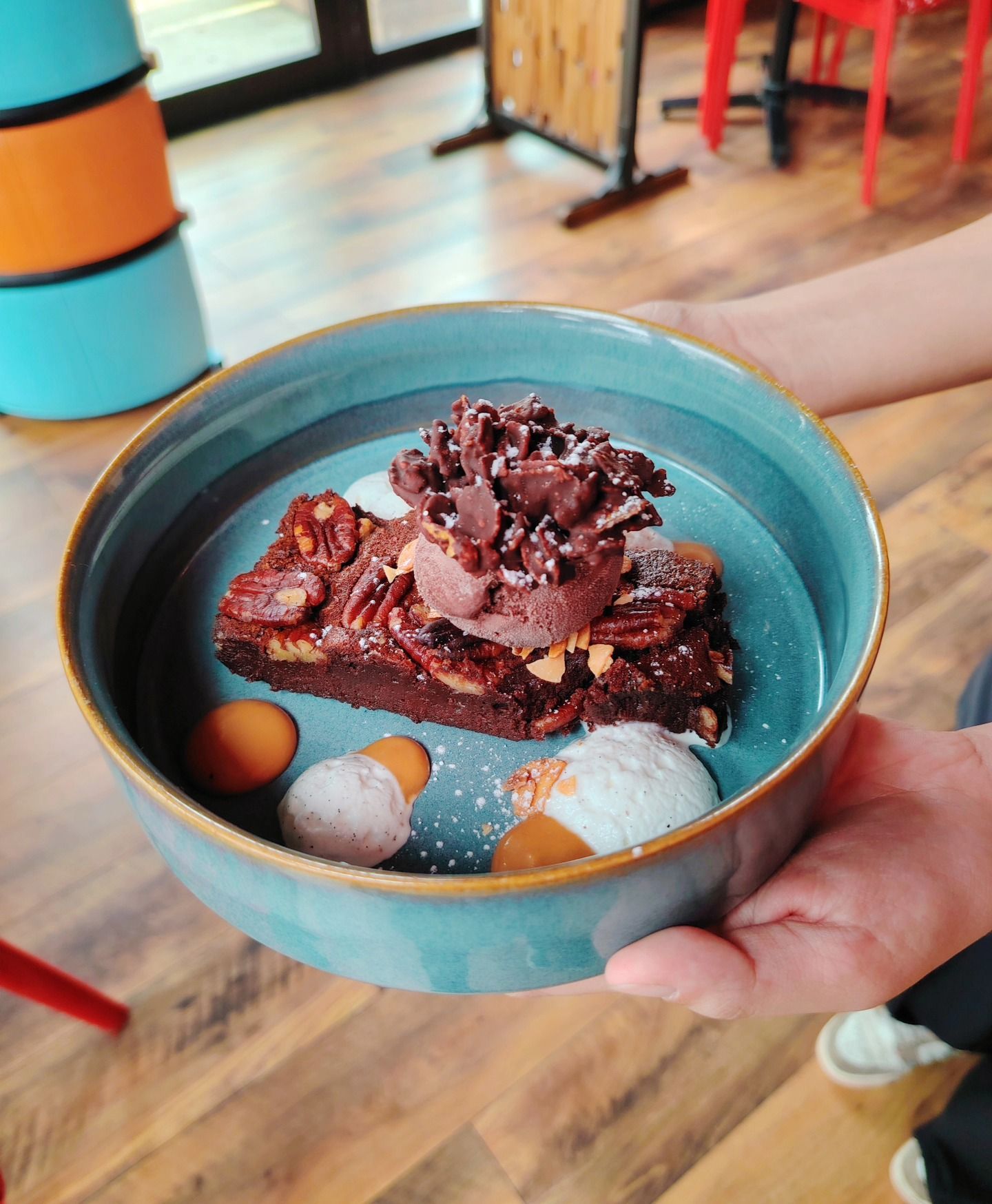Bol bleu contenant un brownie, de la glace, des noix de pécan et des biscuits. Tenu par une personne.
