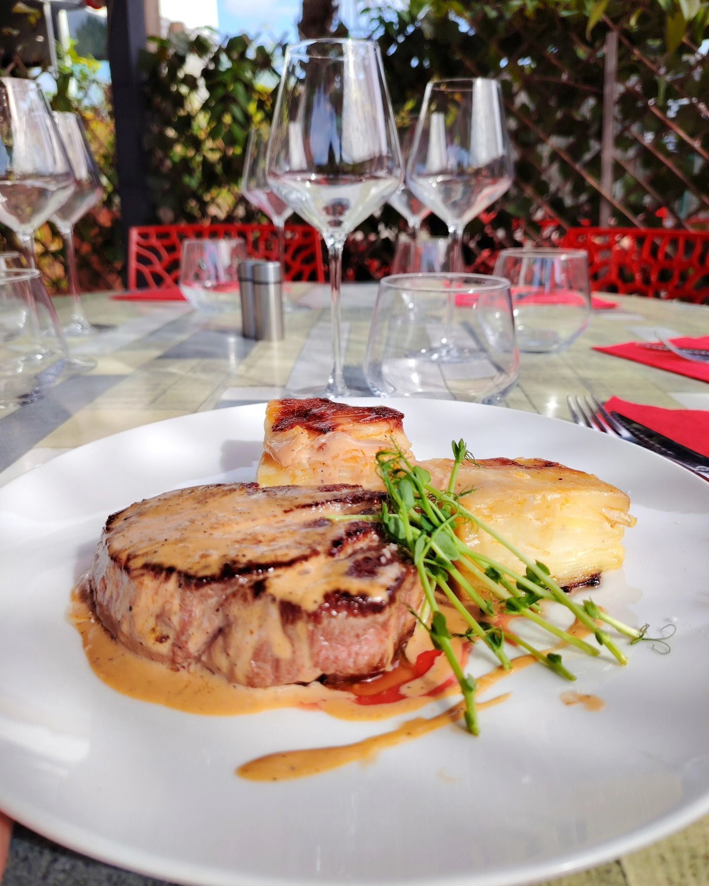 Steak avec sauce et pommes de terre sur une assiette blanche, table de restaurant dressée avec verres à vin.