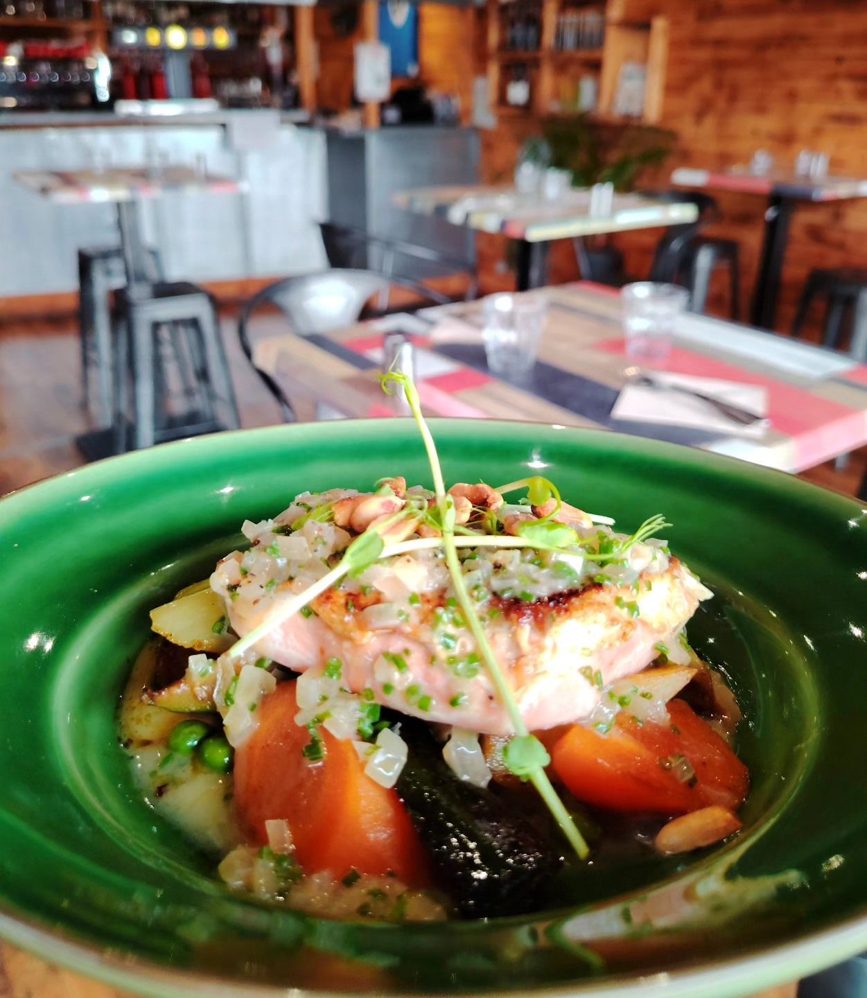 Plat de saumon dans un bol vert, carottes, aubergines, pommes de terre, garniture d'oignons, intérieur de restaurant.