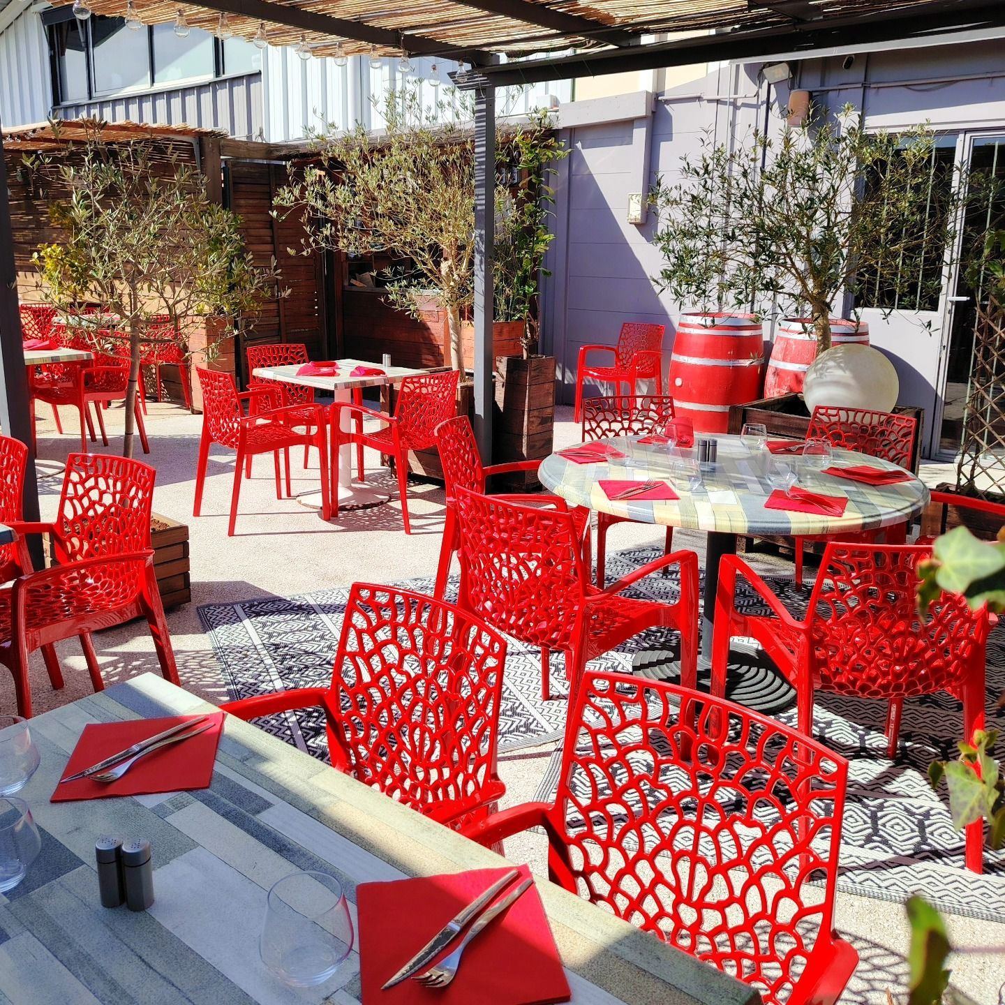 Terrasse extérieure de restaurant avec chaises et tables rouges, tapis à motifs et arbres.