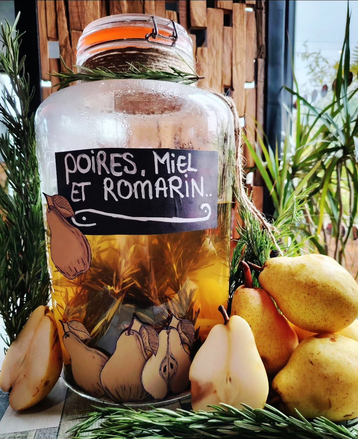 Bocal en verre d'infusion de poire, de miel et de romarin, avec des poires et des brins de romarin.