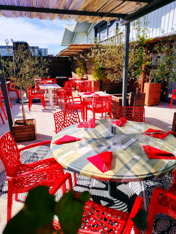 Espace repas extérieur avec chaises et tables rouges sous une pergola.