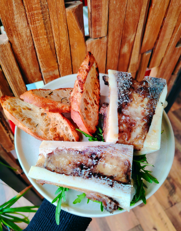 Moelle osseuse rôtie servie avec des tranches de pain grillé sur une assiette garnie de roquette fraîche.