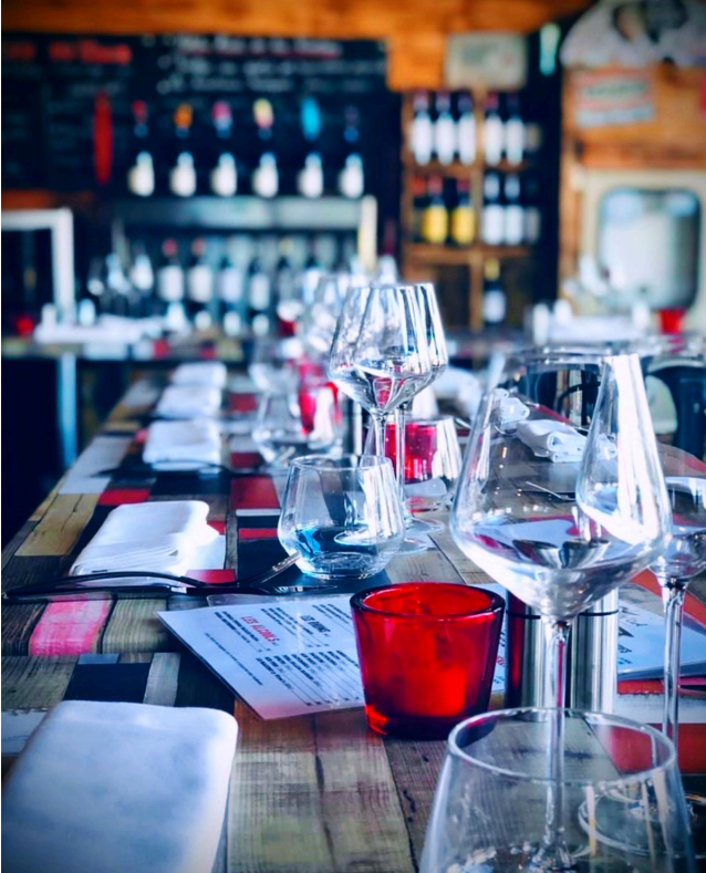 Une table de restaurant dressée avec des verres à vin, des serviettes blanches et des bougies rouges.