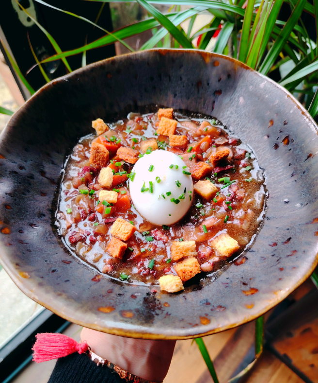 Un bol rustique de ragoût de haricots rouges garni de croûtons, d'herbes fraîches et d'un œuf mollet entier.