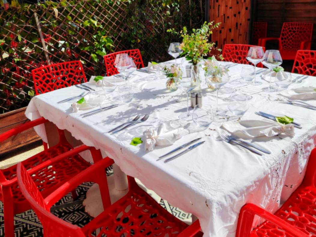 Des chaises rouges entourent une table carrée dressée avec une nappe blanche, des couverts, des verres et des centres de table floraux.