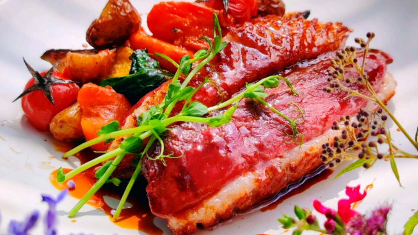 Magret de canard poêlé servi avec des tomates et des légumes rôtis, garni de verdure fraîche sur une assiette blanche.