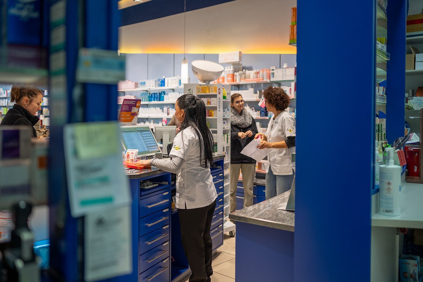 Apotheker helfen Kunden in einer Apotheke mit blau-weißem Dekor.