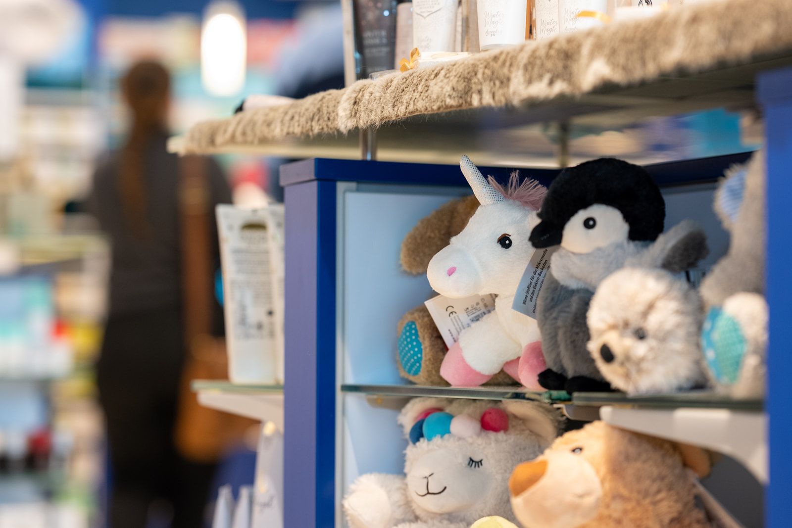 Regale mit Stofftieren in einem Geschäft. Im Hintergrund ist eine Person unscharf.