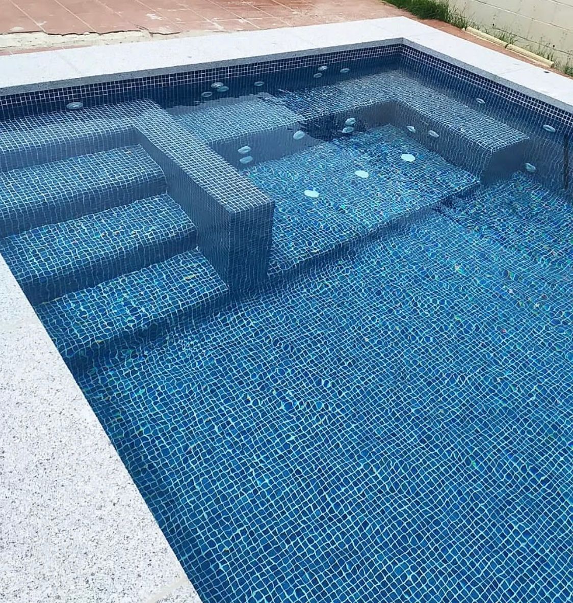 Una piscina con azulejos azules y escaleras.