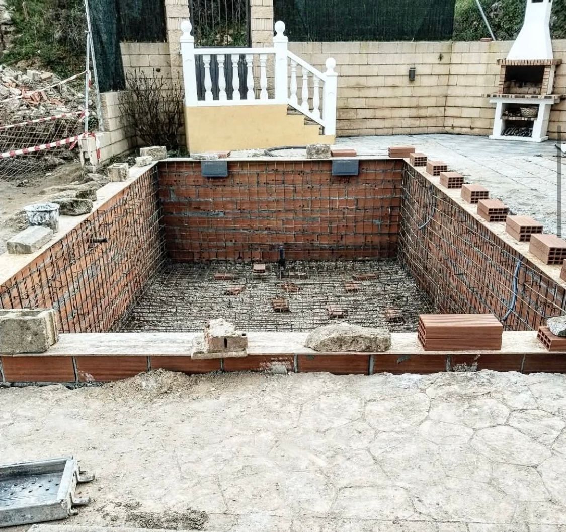 Se está construyendo una gran piscina de ladrillo en un patio trasero.