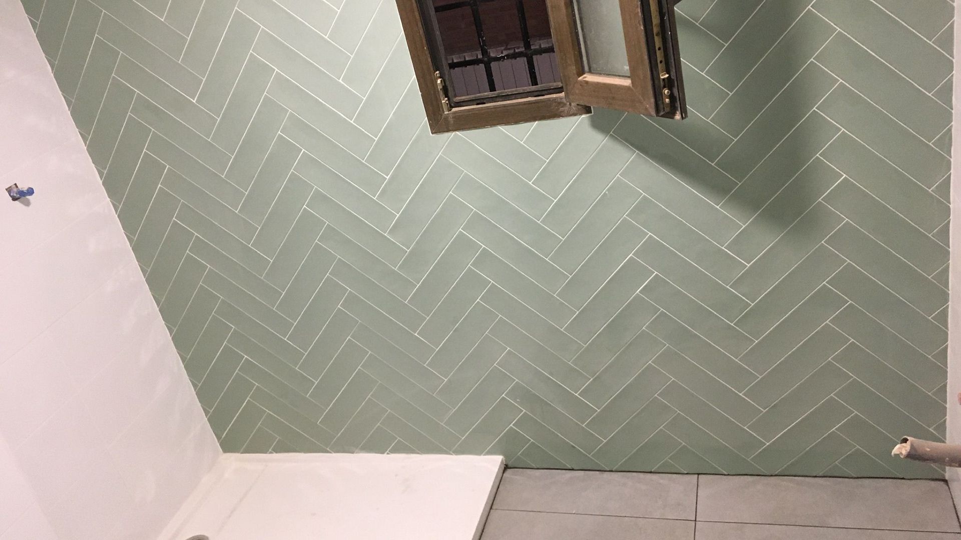 Azulejo verde en espiga en una pared con una pequeña ventana. La habitación está en proceso de renovación