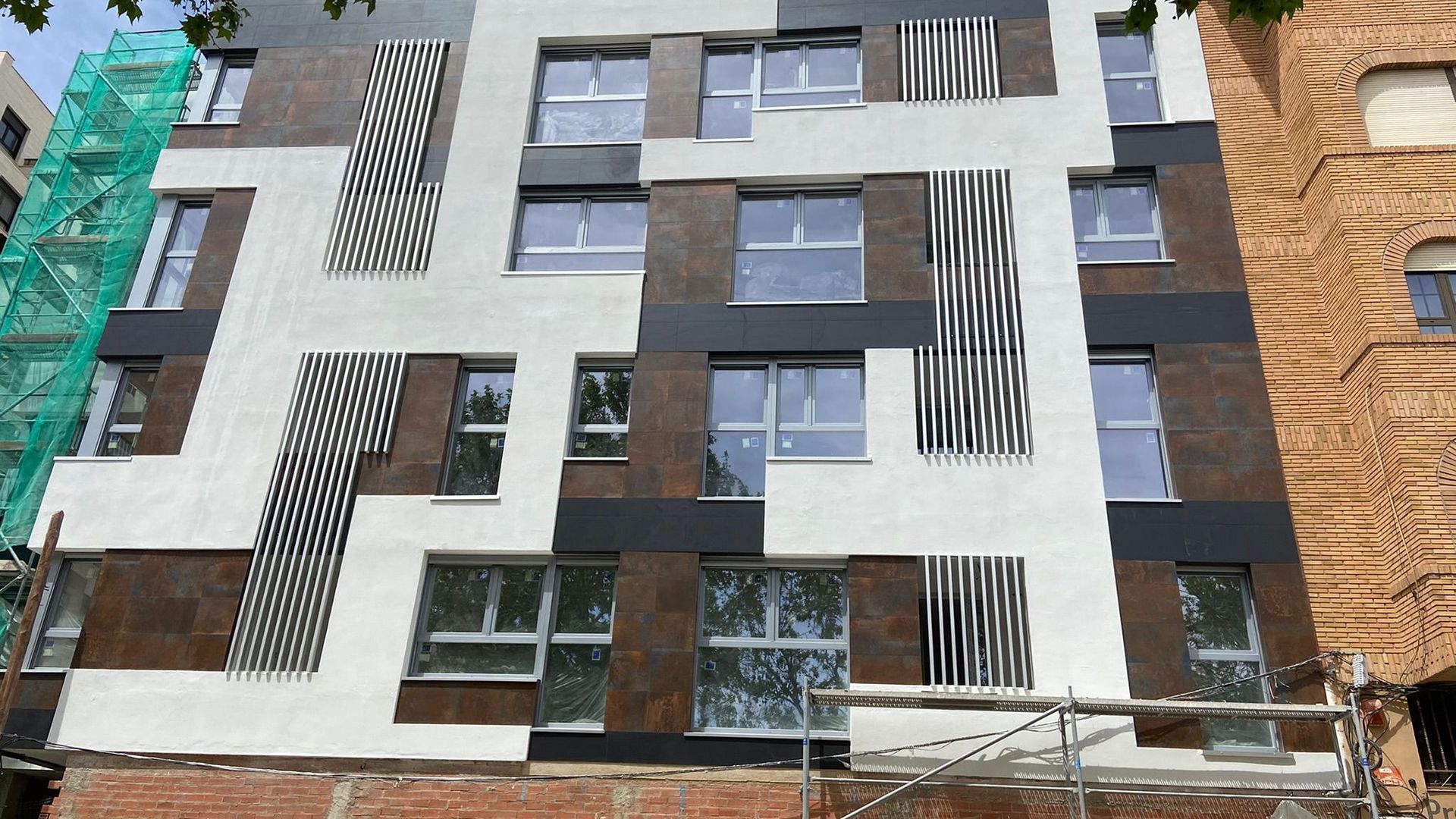 Fachada de edificio moderno con patrones geométricos en paneles marrones, blancos, negros y rayados